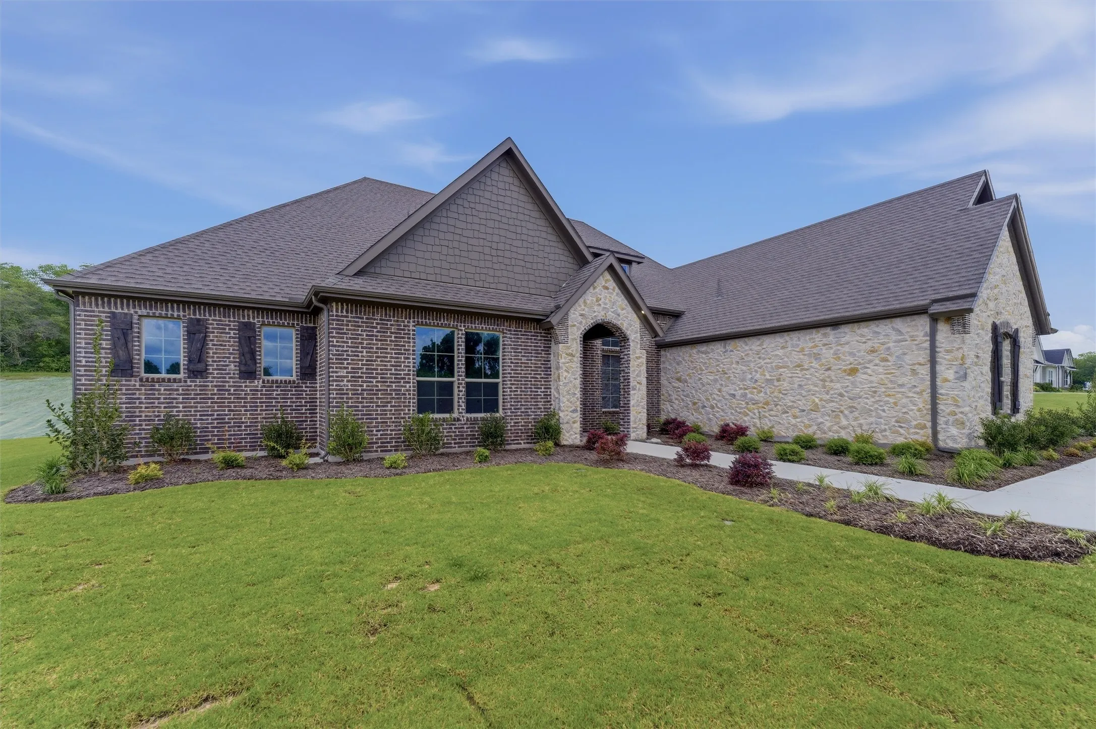 Brick and stone exterior featuring an arched entry, shingle roof, dark-framed windows, and decorative shutters