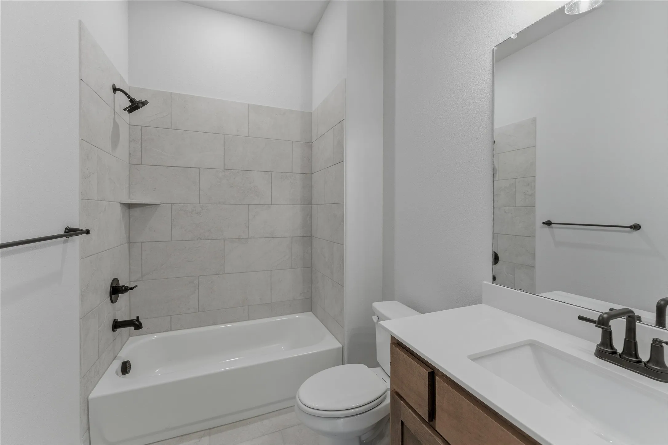 Bathroom featuring a white tub and shower combination with light-toned tiled surround, an integrated shower niche, and matte black fixtures