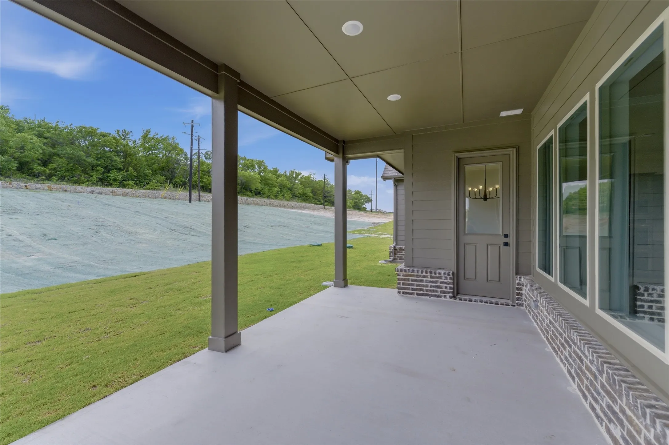 Covered patio with a smooth concrete surface, recessed lighting, and a painted wood-frame door with a glass insert