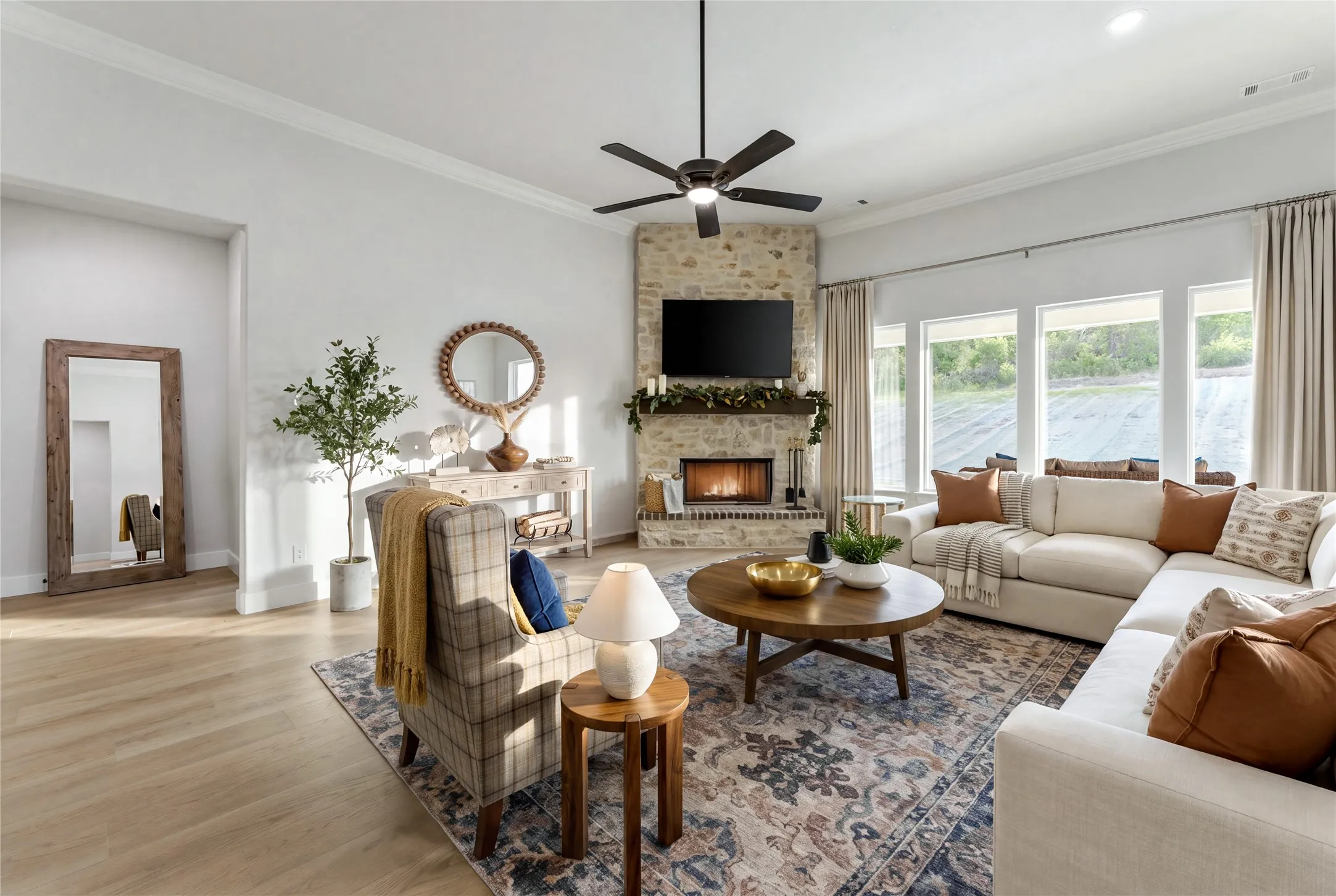 Spacious living area featuring light wood-finish flooring, a stone-clad fireplace, and multiple large windows