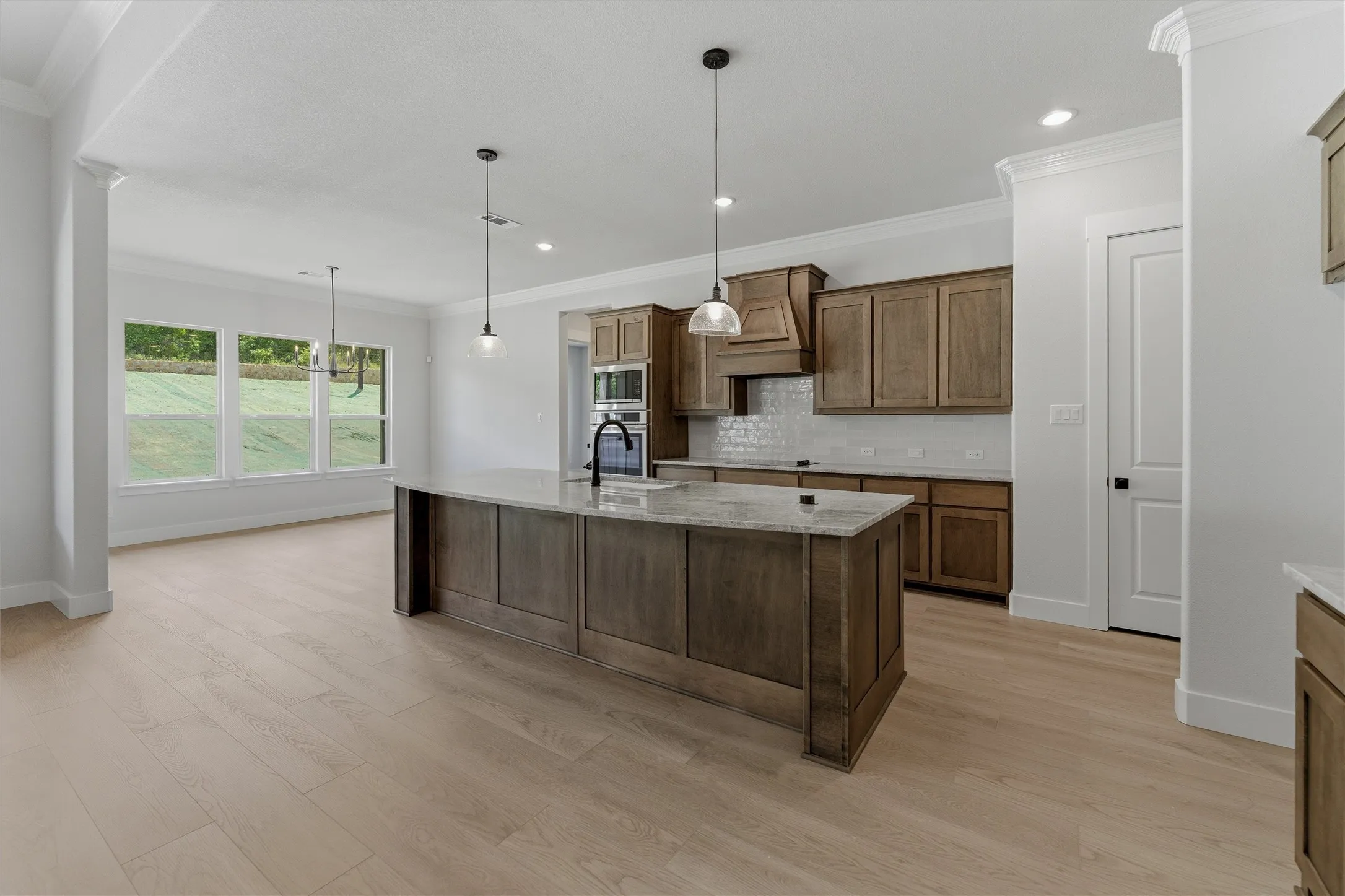 Open-concept kitchen featuring a central island with a stone countertop, wood-finish cabinetry, built-in appliances, and light wood-finish flooring