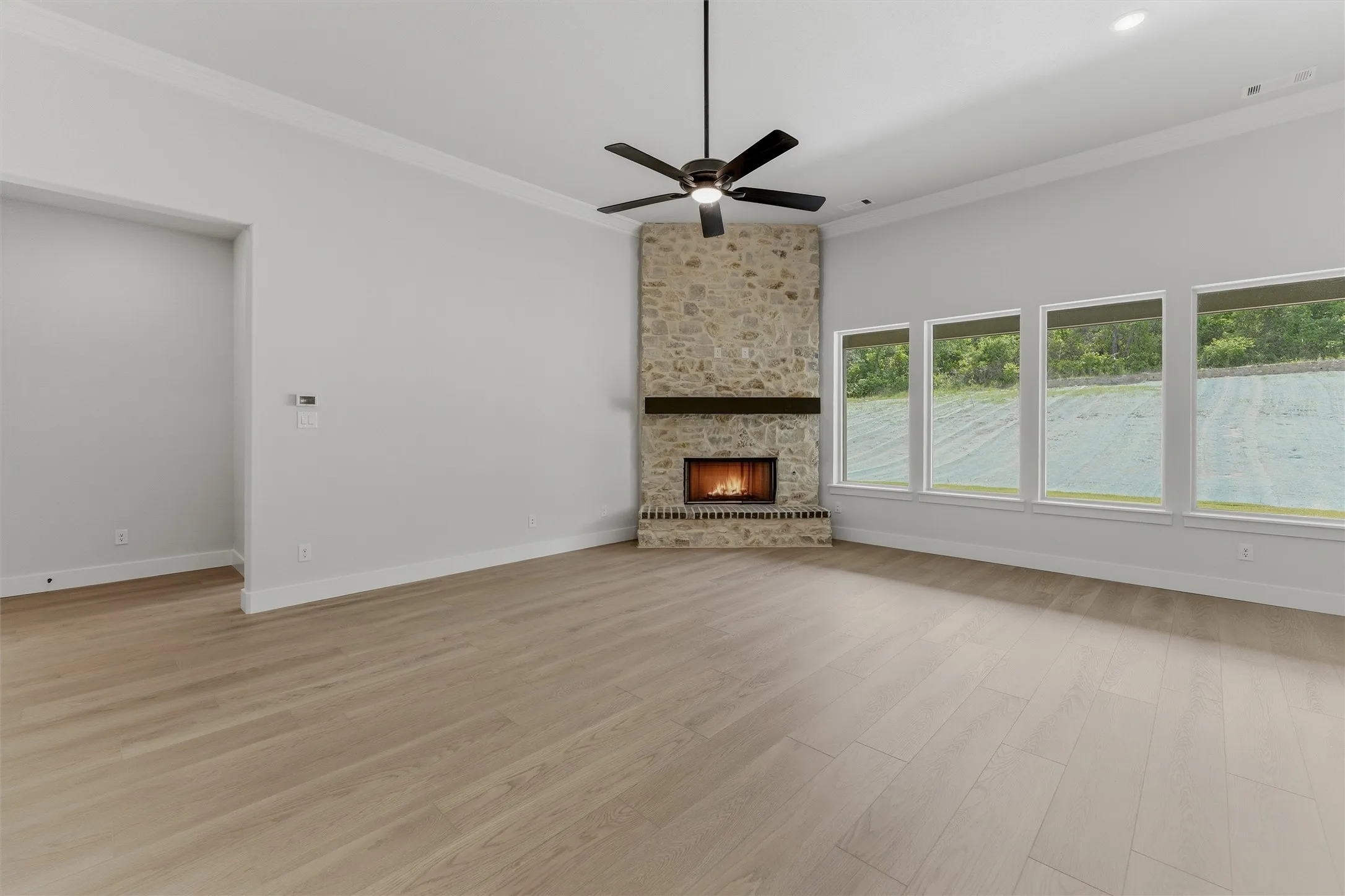Spacious room featuring a stone fireplace with a wood mantle, wood-finish flooring, a ceiling fan, and a wall of four windows