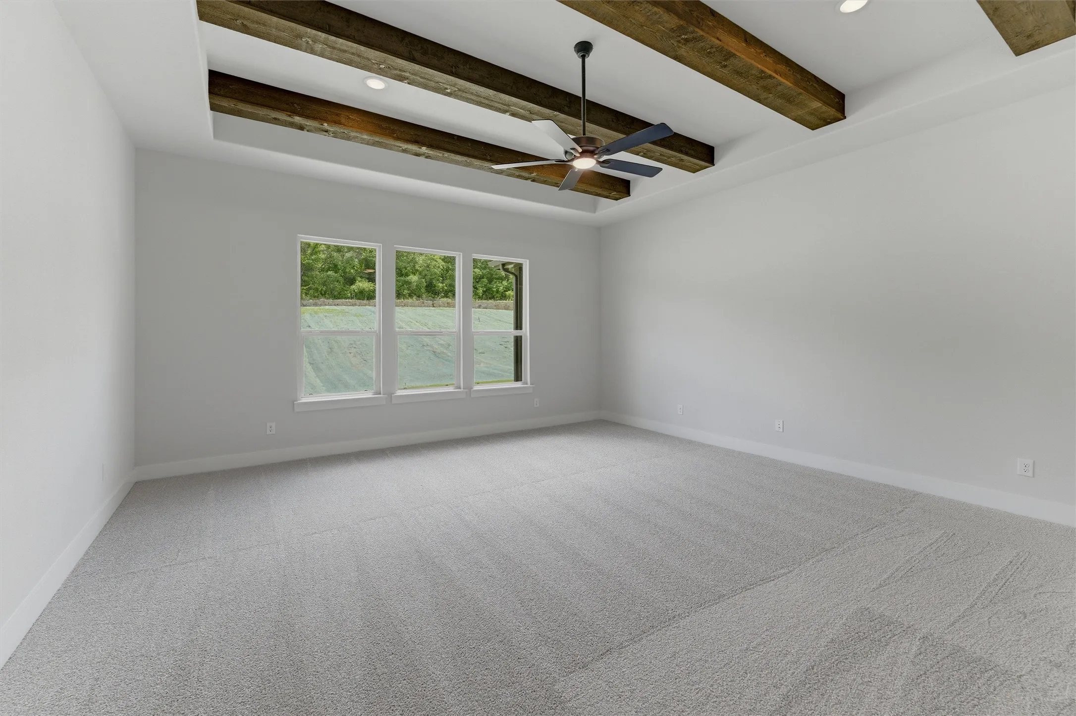 Spacious room featuring a tray ceiling with exposed wood beams, a ceiling fan, and recessed lighting