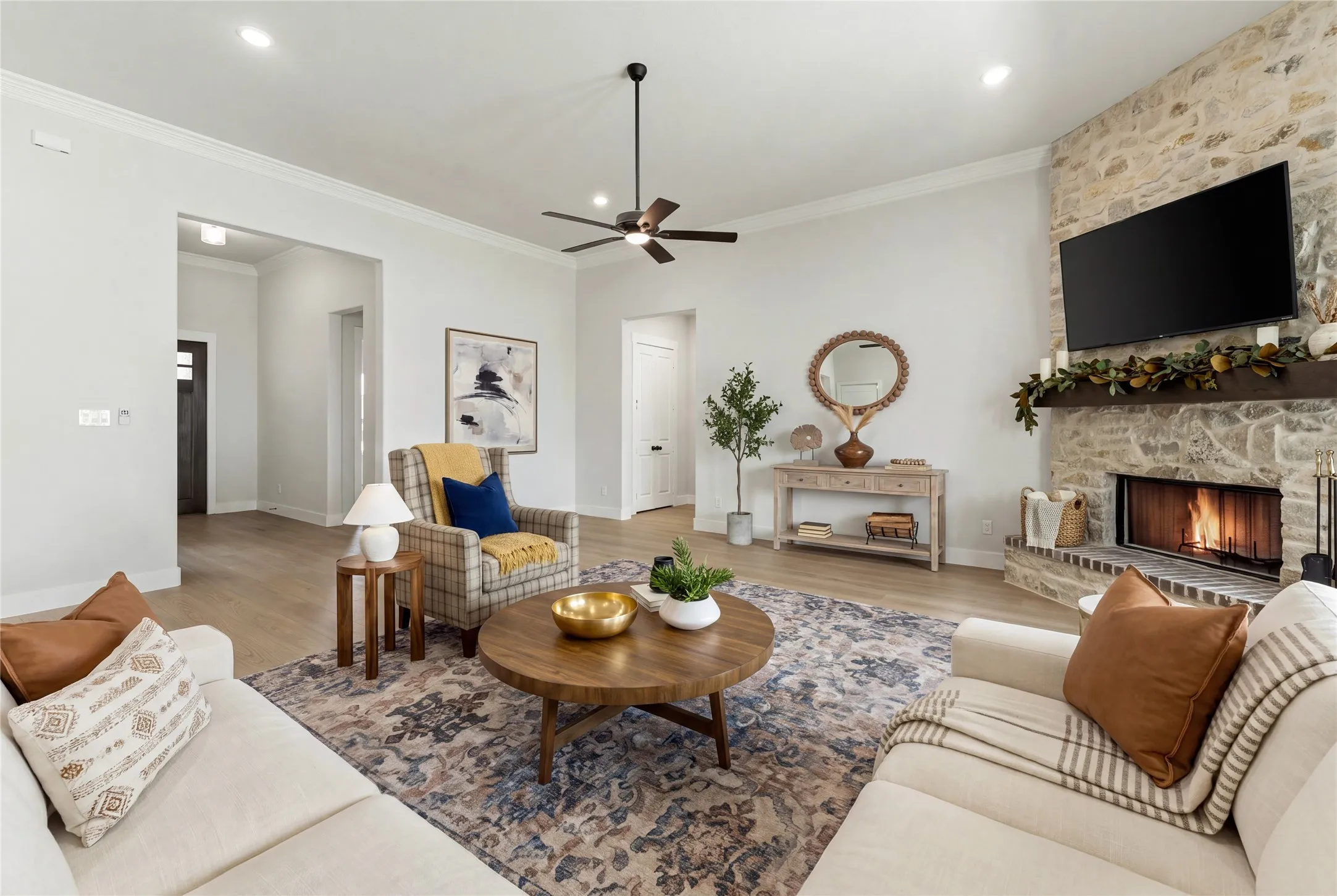 Spacious living area featuring a stone-clad fireplace with a substantial wood mantel, crown molding, recessed lighting, and wood-finish flooring