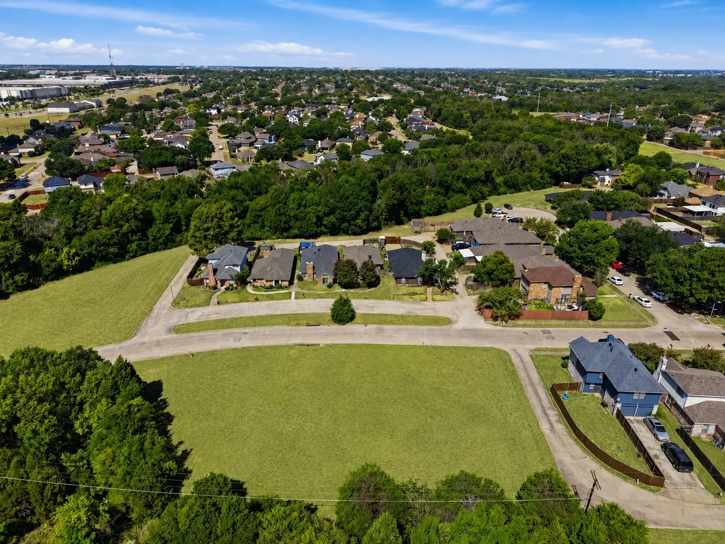 Expansive grassy lot bordered by mature trees and paved roadways