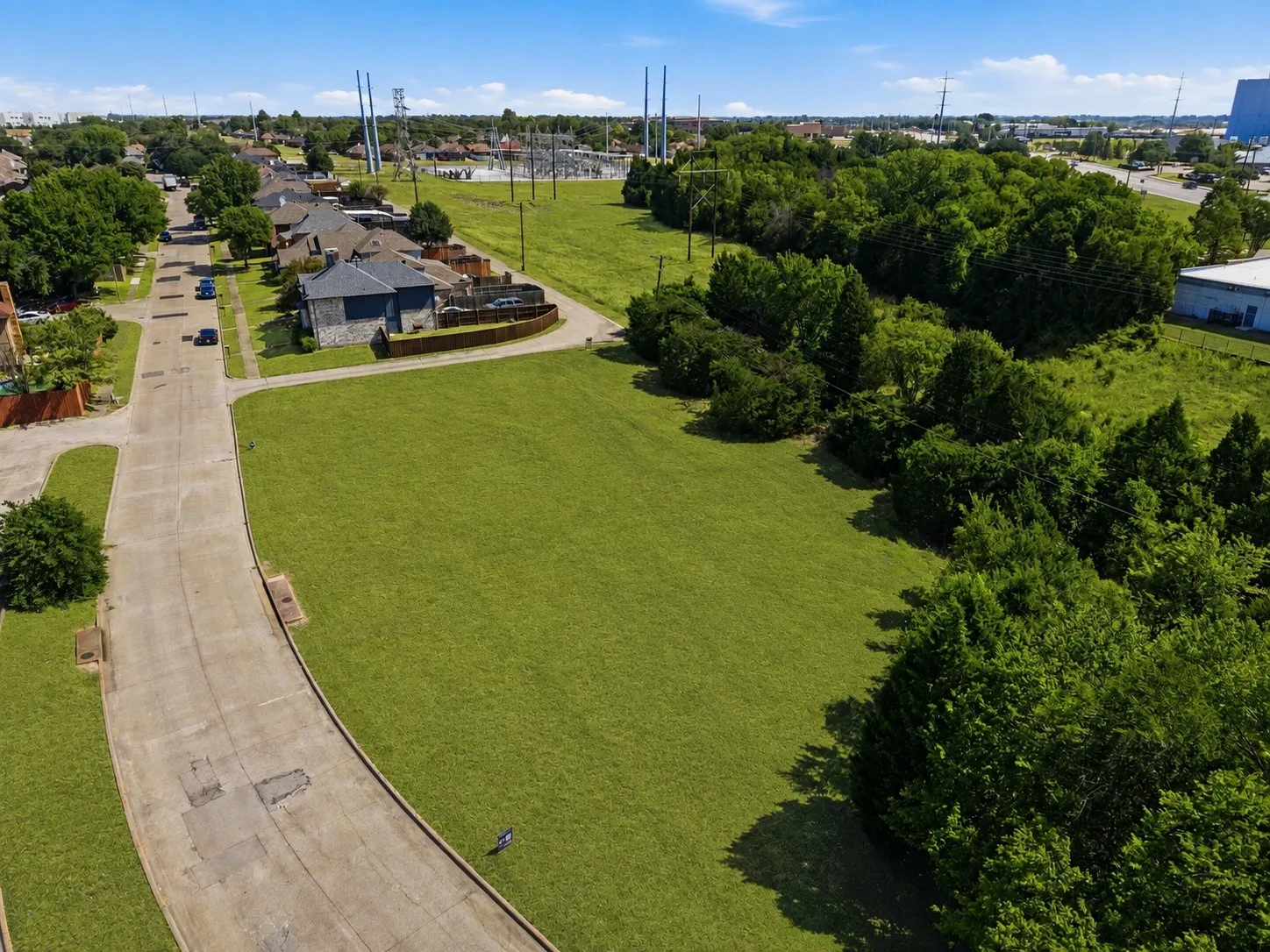 Expansive grassy lot bordered by mature trees and paved roadways