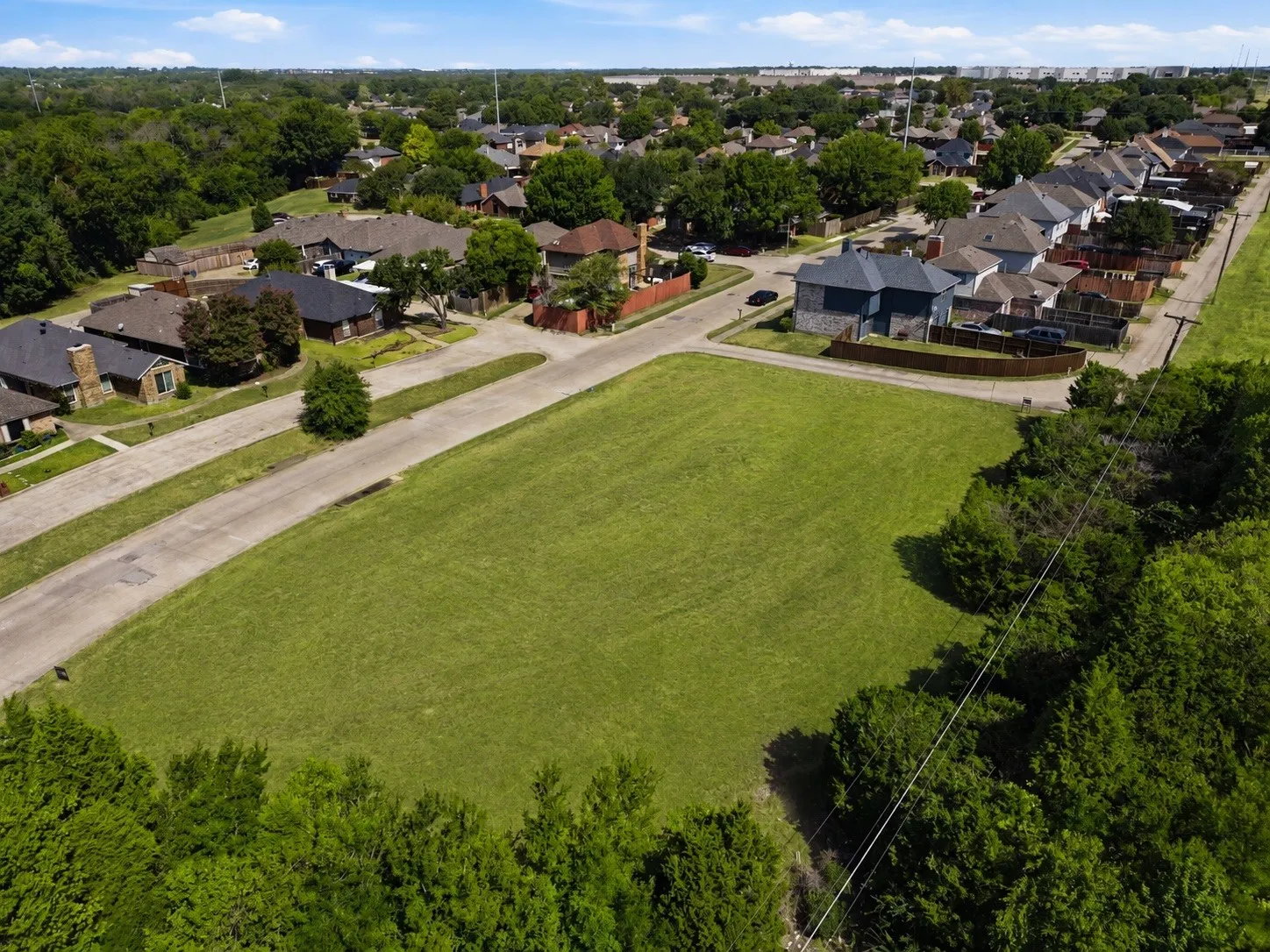 Expansive grassy lot bordered by mature trees and paved roadways
