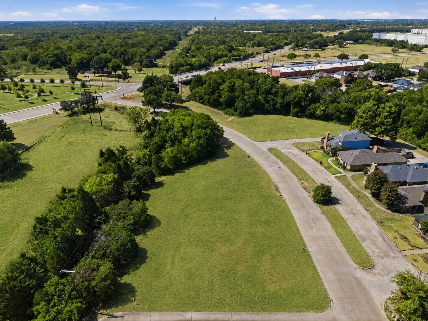 Expansive grassy lot bordered by mature trees and paved roadways