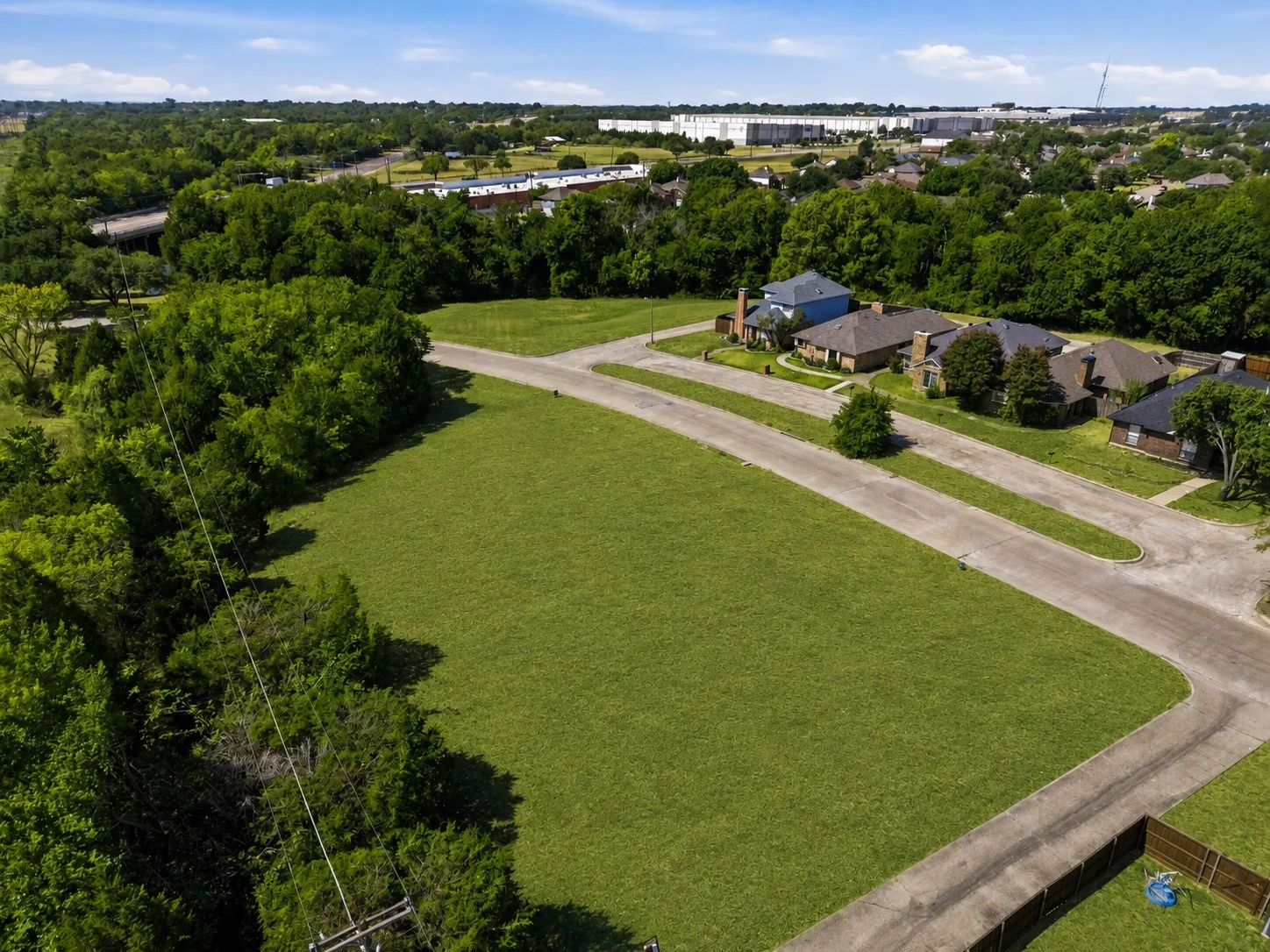 Expansive grassy lot bordered by mature trees and paved roadways