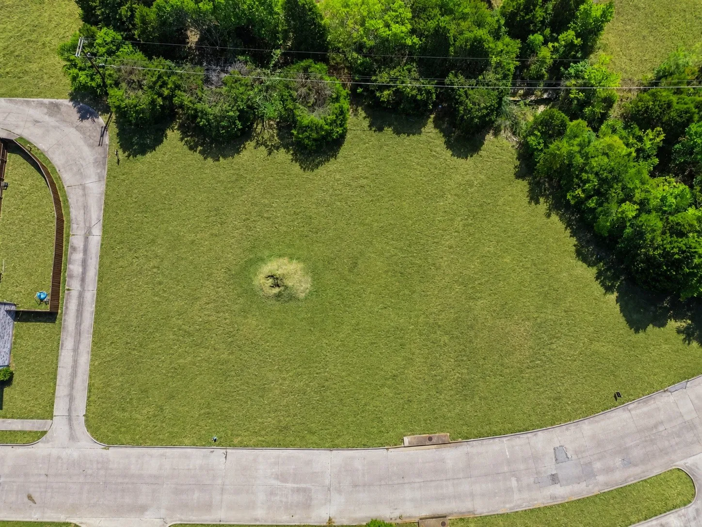 Expansive grassy lot bordered by mature trees and paved roadways
