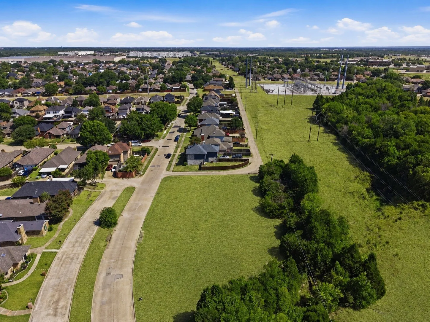 Expansive grassy lot bordered by mature trees and paved roadways