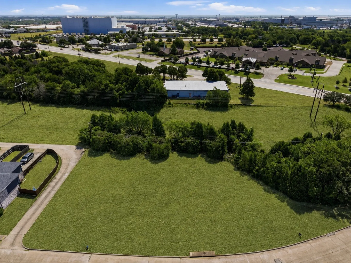 Expansive grassy lot bordered by mature trees and paved roadways