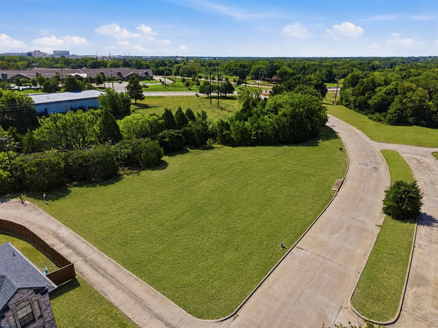Expansive grassy lot bordered by mature trees and paved roadways