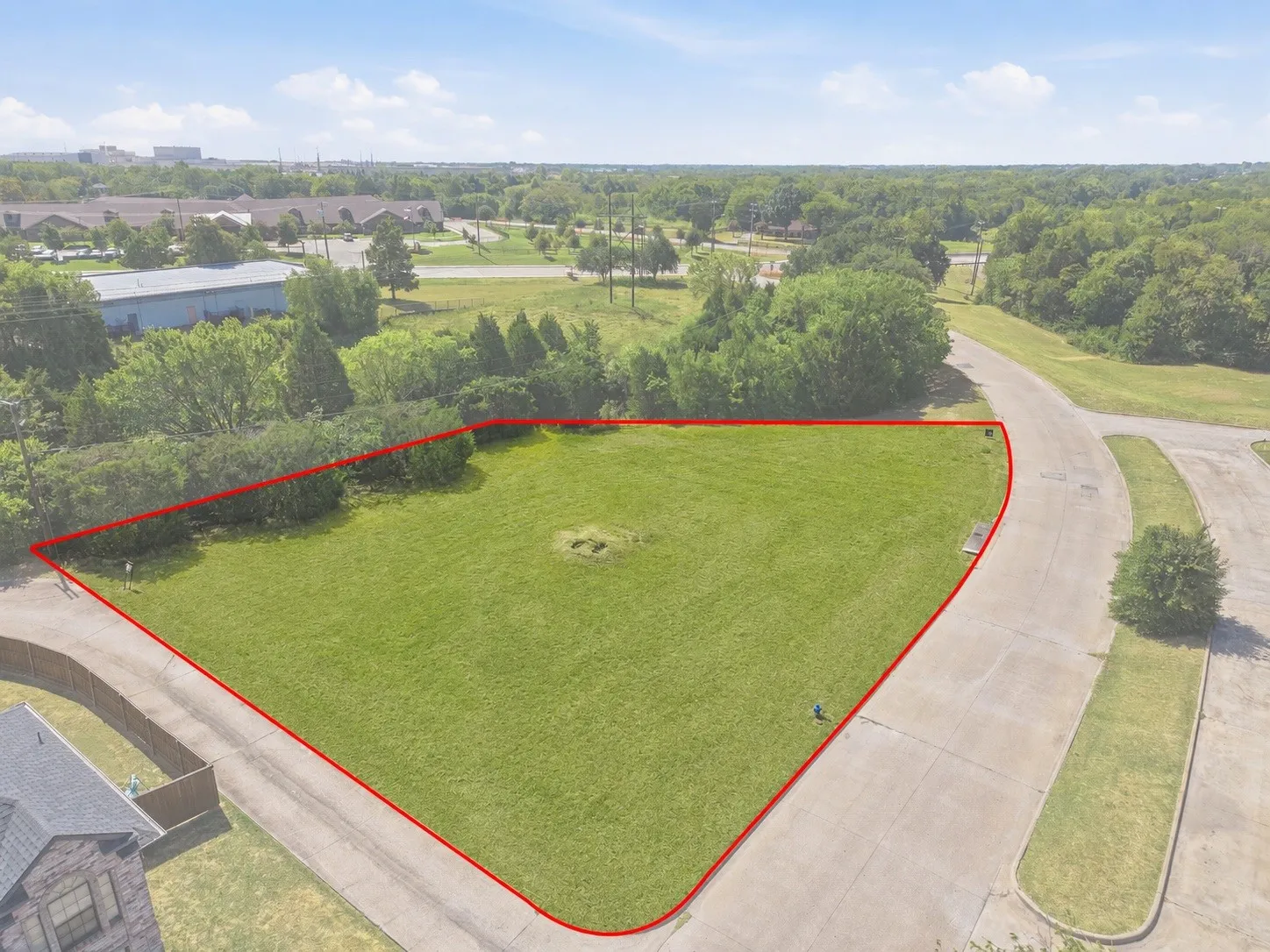 Expansive grassy lot bordered by mature trees and paved roadways