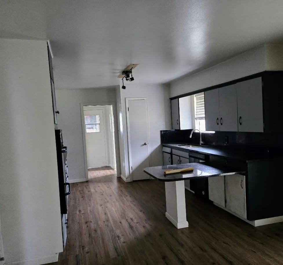 Kitchen with dark countertops, dark wood finished floors, gray cabinetry, a peninsula, and dishwasher
