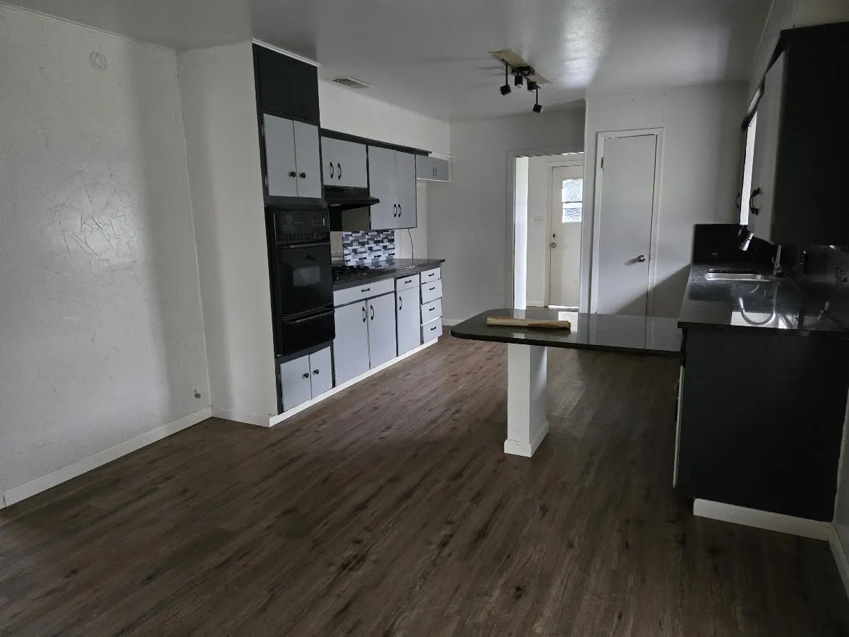 Kitchen featuring dark wood finished floors, black oven, white cabinetry, decorative backsplash, and a warming drawer