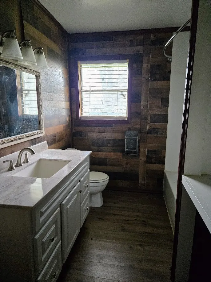 Full bathroom with vanity, dark wood-style floors, wood walls, and  shower combination