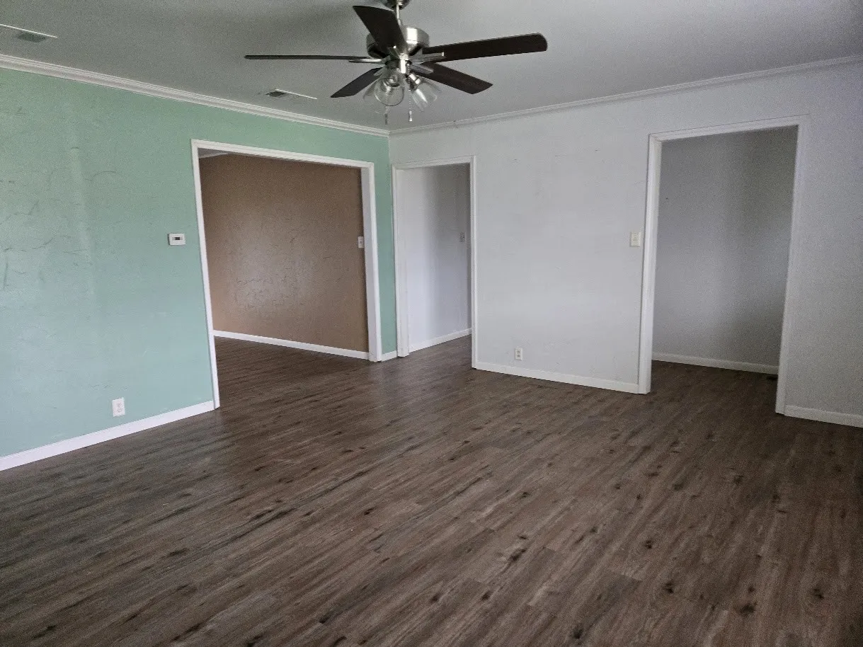 Unfurnished living room with ornamental molding, dark wood-style floors, and ceiling fan