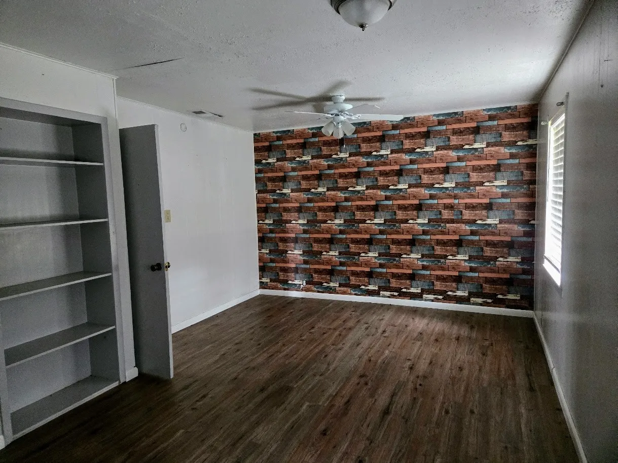 Empty room with dark wood-style floors, a textured ceiling, ceiling fan, and an accent wall