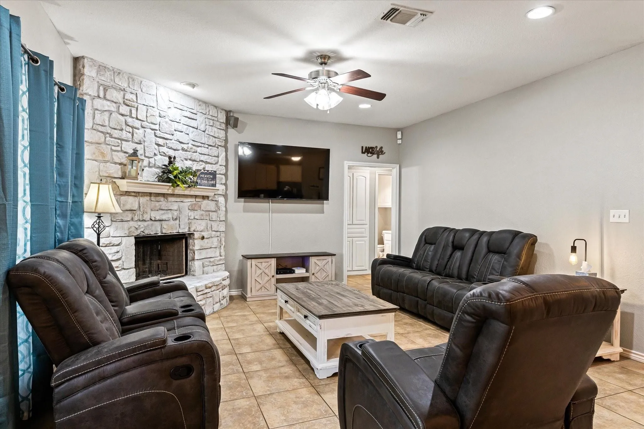 Living room featuring visible vents, a ceiling fan, light tile patterned floors, and a fireplace