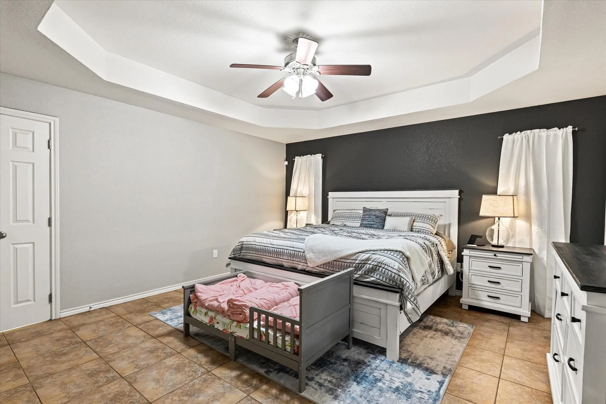 Bedroom featuring light tile patterned floors, a tray ceiling, baseboards, and a ceiling fan
