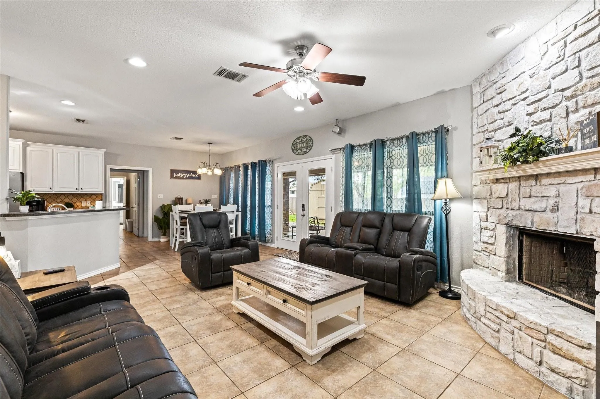 Living room with a fireplace, light tile patterned floors, french doors, visible vents, and ceiling fan with notable chandelier