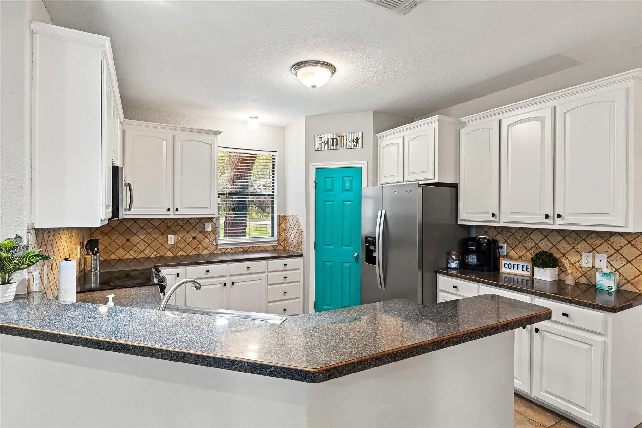Kitchen with a peninsula, backsplash, dark countertops, stainless steel appliances, and a sink