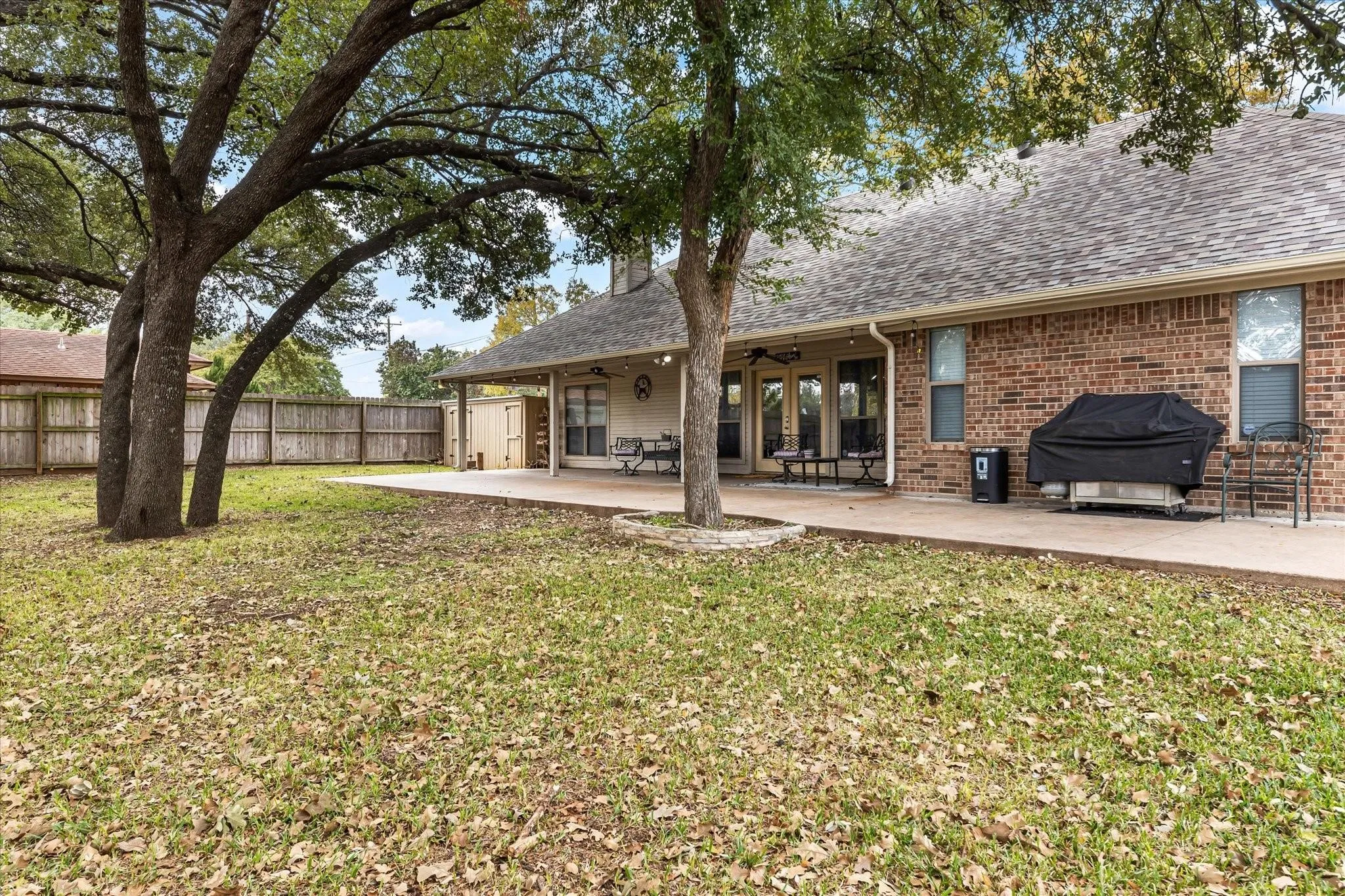 Rear view of house featuring roof with shingles, a patio area, brick siding, and fence
