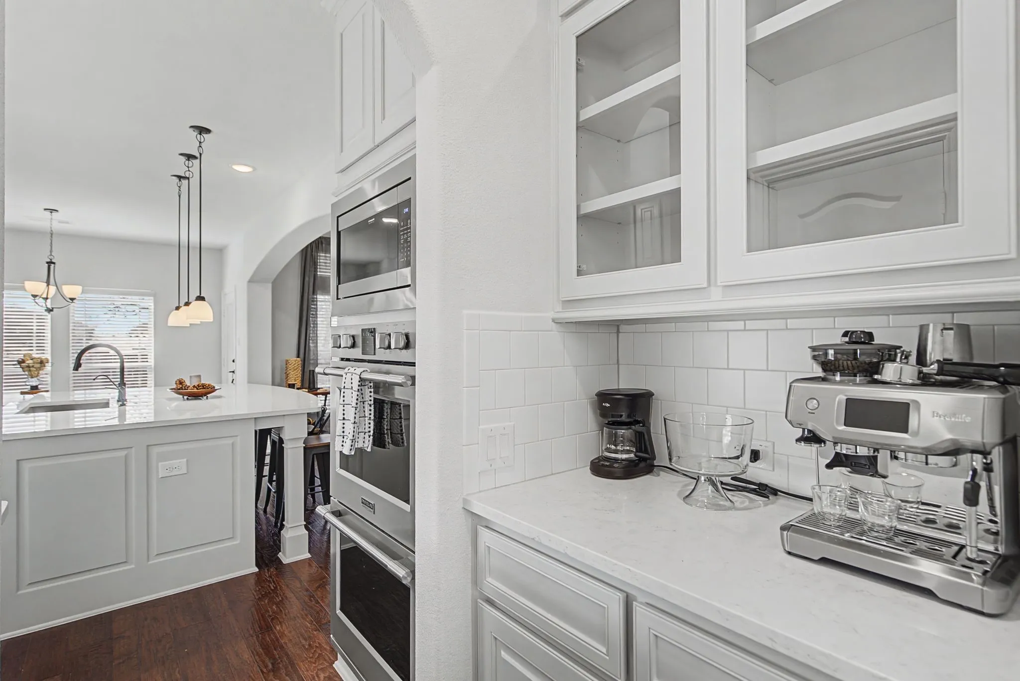 Kitchen with white cabinetry, stainless steel appliances, light stone countertops, dark wood finished floors, and glass fronted cabinets