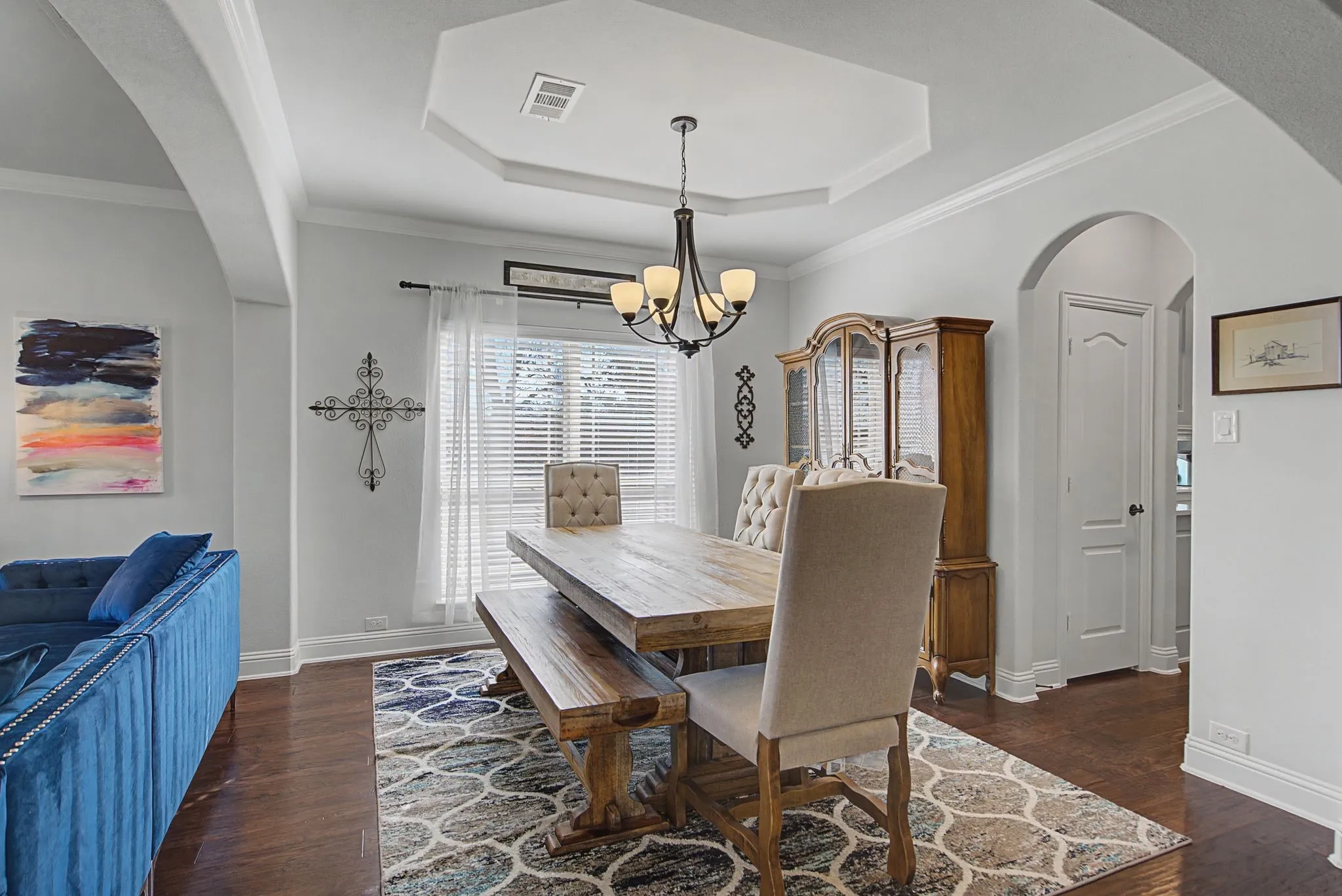 Dining space featuring arched walkways, suspended lighting, dark wood-style floors, ornamental molding, and a tray ceiling