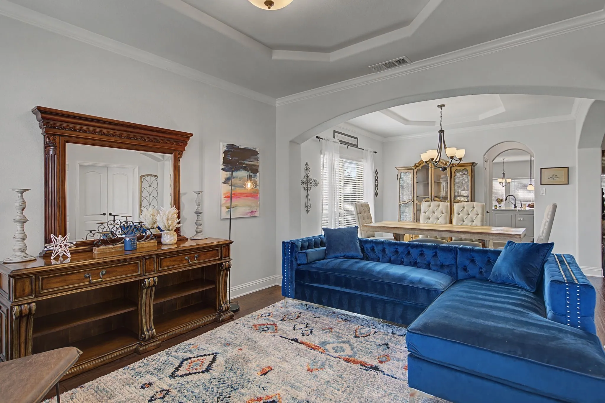Living area with a tray ceiling, hanging lights, dark wood-type flooring, arched walkways, and ornamental molding