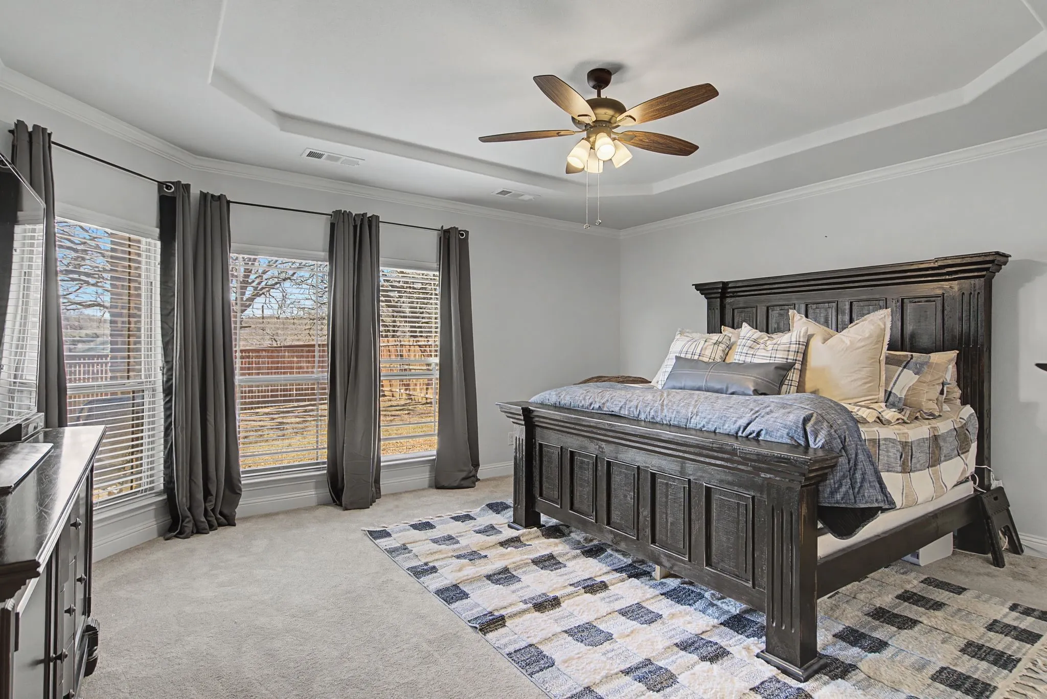 Bedroom featuring a raised ceiling, light carpet, a ceiling fan, and ornamental molding