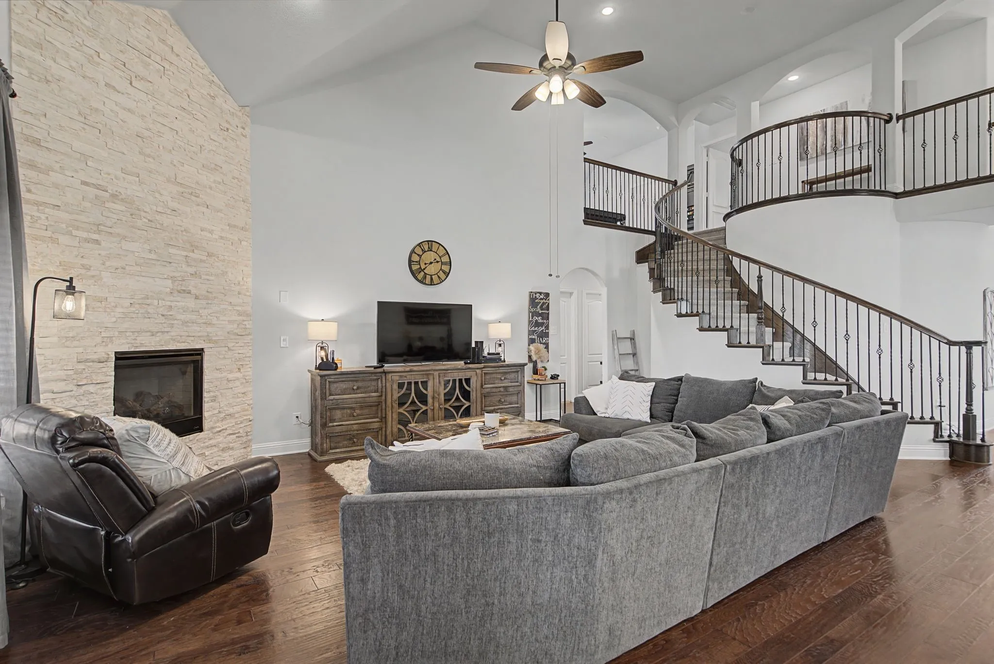 Living area featuring arched walkways, dark wood-style floors, ceiling fan, a stone fireplace, and recessed lighting