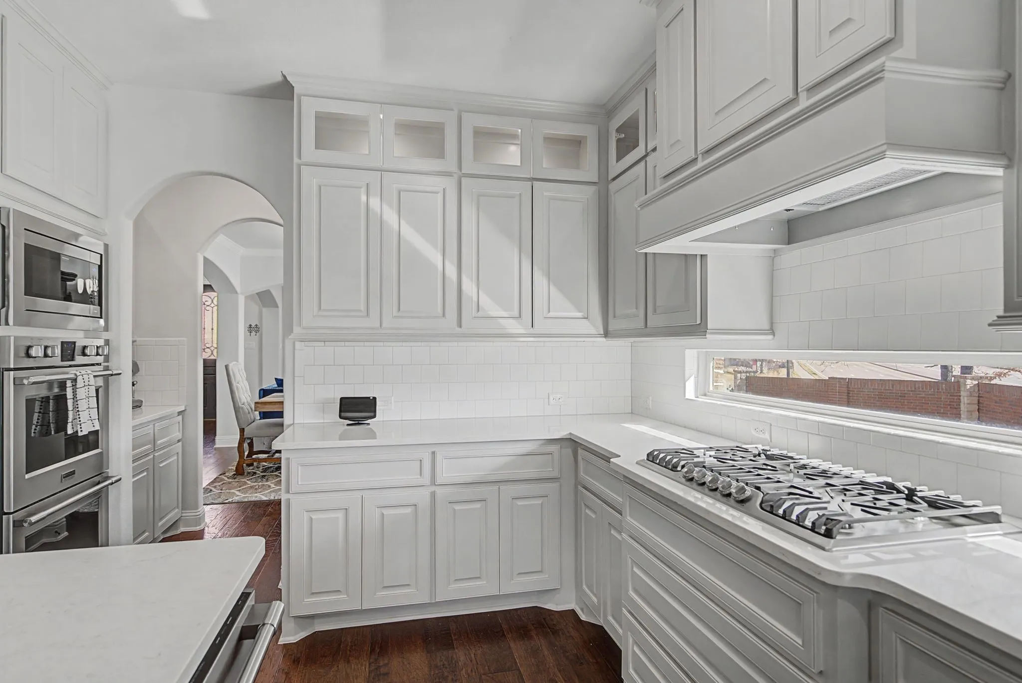 Kitchen featuring dark wood-type flooring, stainless steel appliances, arched walkways, glass fronted cabinets, and white cabinets