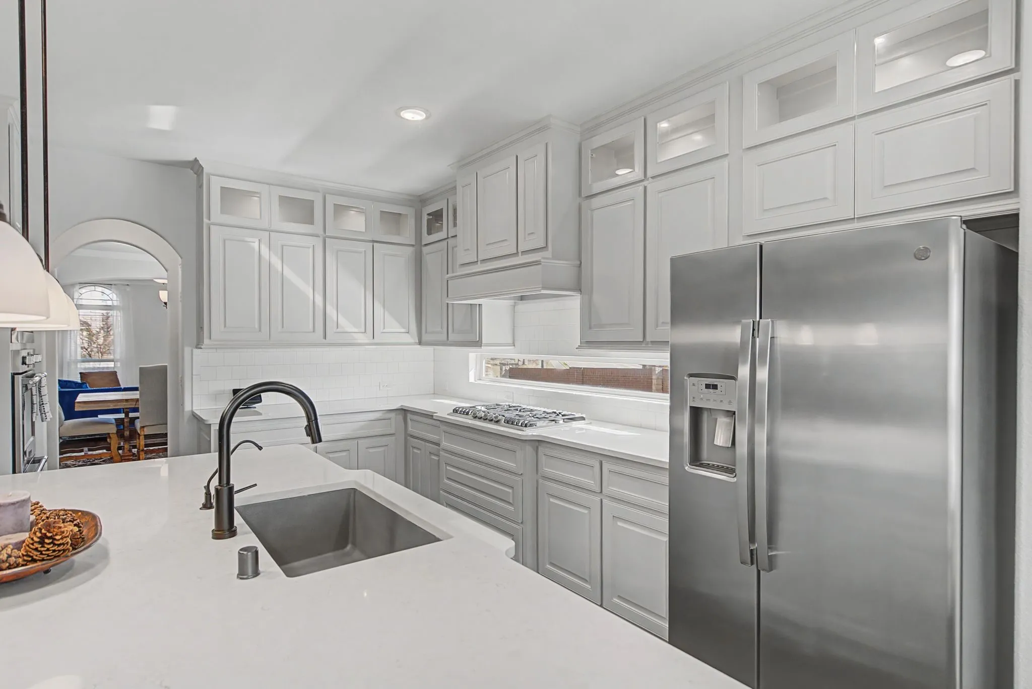 Kitchen with stainless steel appliances, glass insert cabinets, light stone counters, arched walkways, and recessed lighting