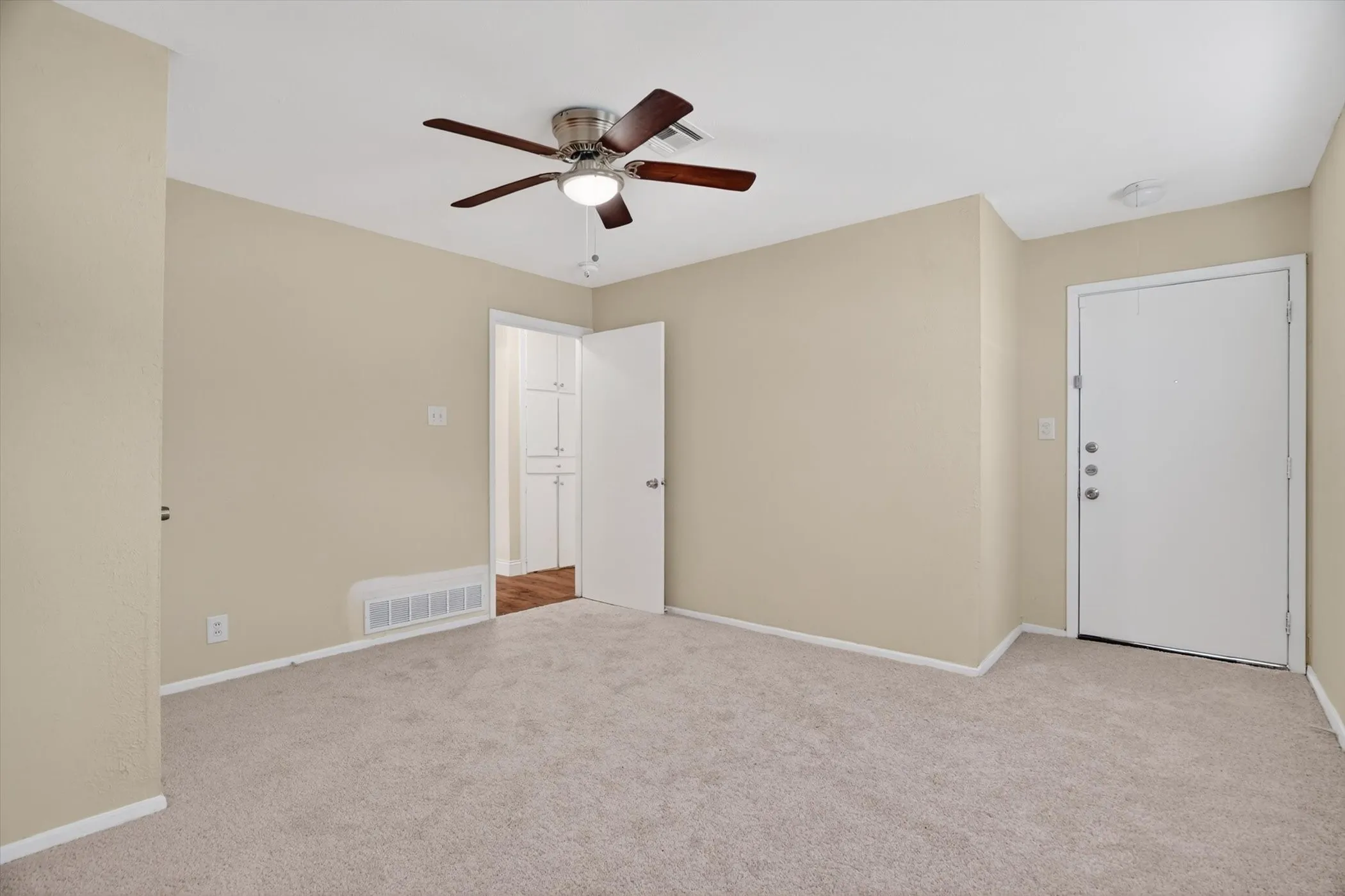 Neutral tone wall paint, light-colored carpeting, white baseboards, and a ceiling fan with integrated lighting