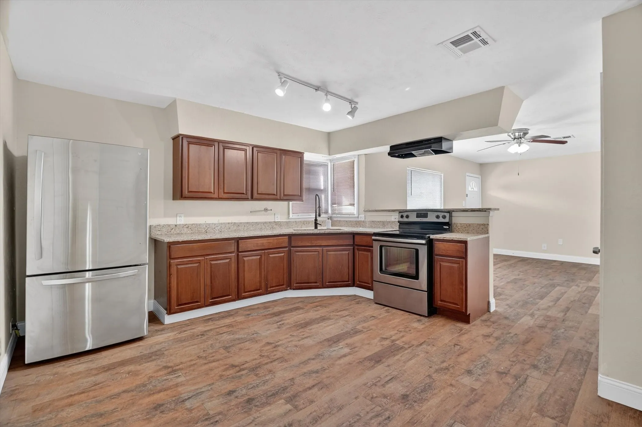 Kitchen featuring stainless steel appliances, wood-finish flooring, rich wood cabinetry, light-toned countertops, and a ceiling fan