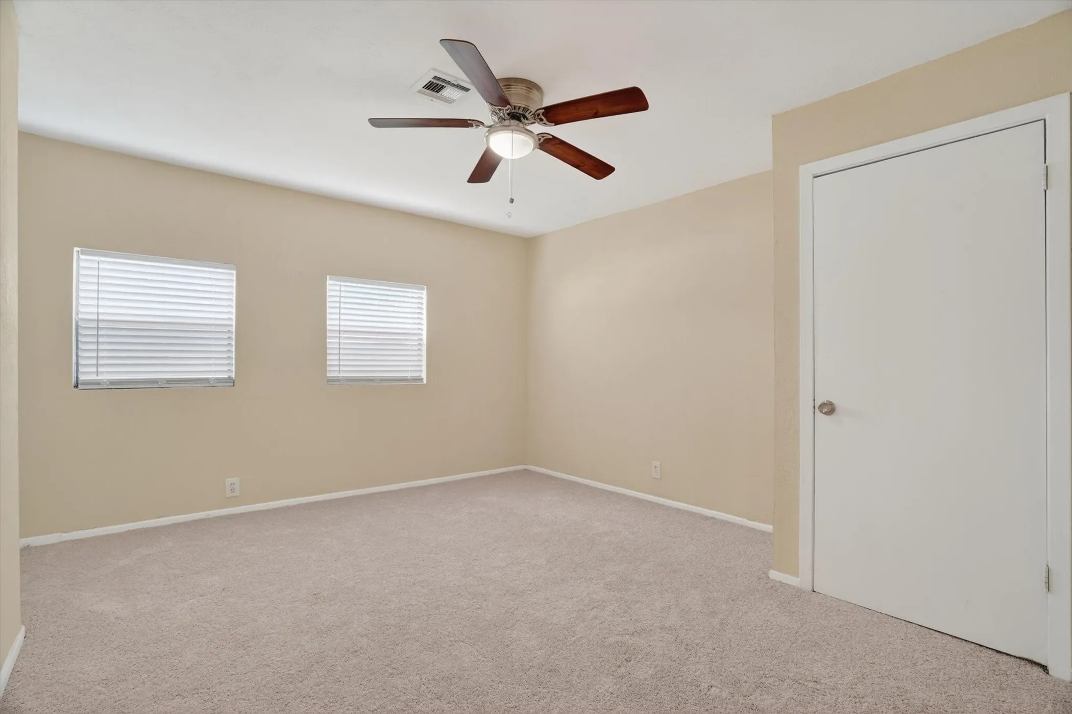 Neutral-toned room featuring two windows with horizontal blinds, a ceiling fan with light fixture, and plush carpeting
