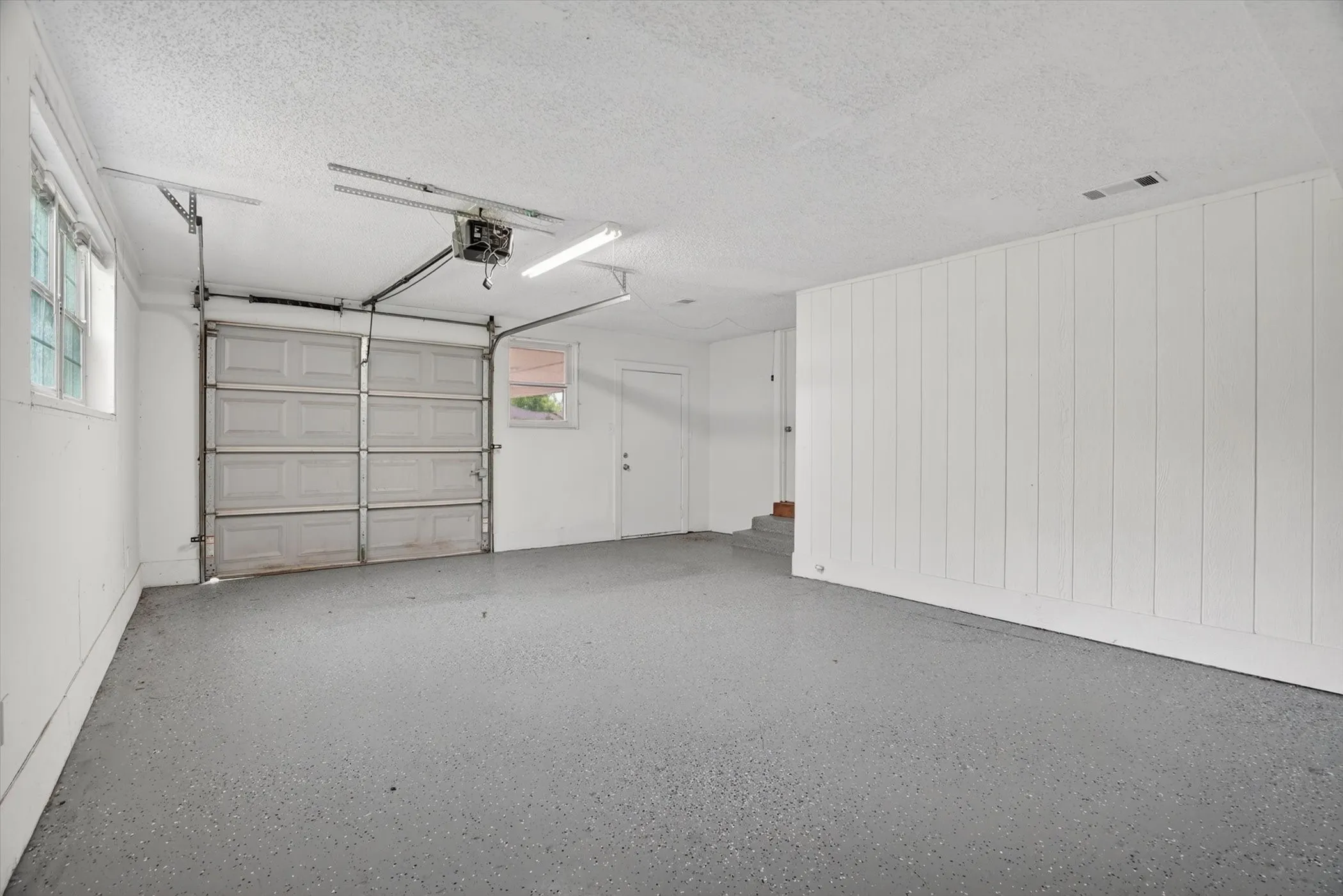 Spacious garage featuring a durable epoxy-coated floor, automatic garage door opener, two windows for natural light, and a dedicated utility door