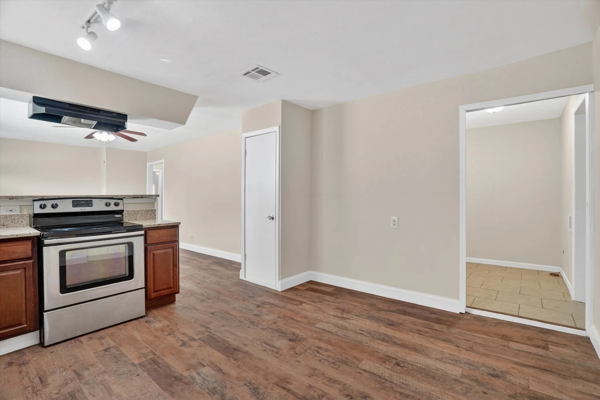 Kitchen area featuring stainless steel range, rich wood-finish cabinetry, light-toned granite-style countertops, wood-finish flooring, and track lighting