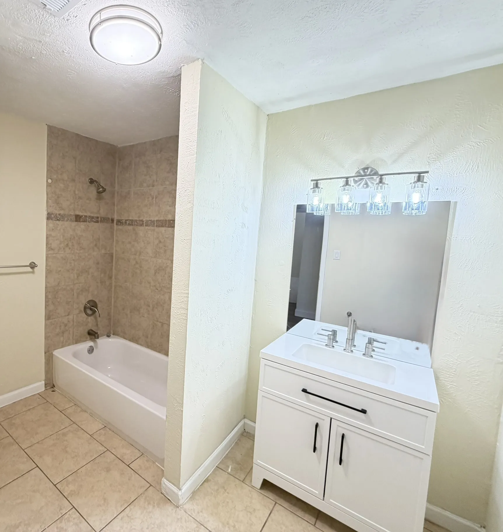 White vanity with brushed nickel hardware, integrated sink, and wall-mounted mirror with decorative light fixture