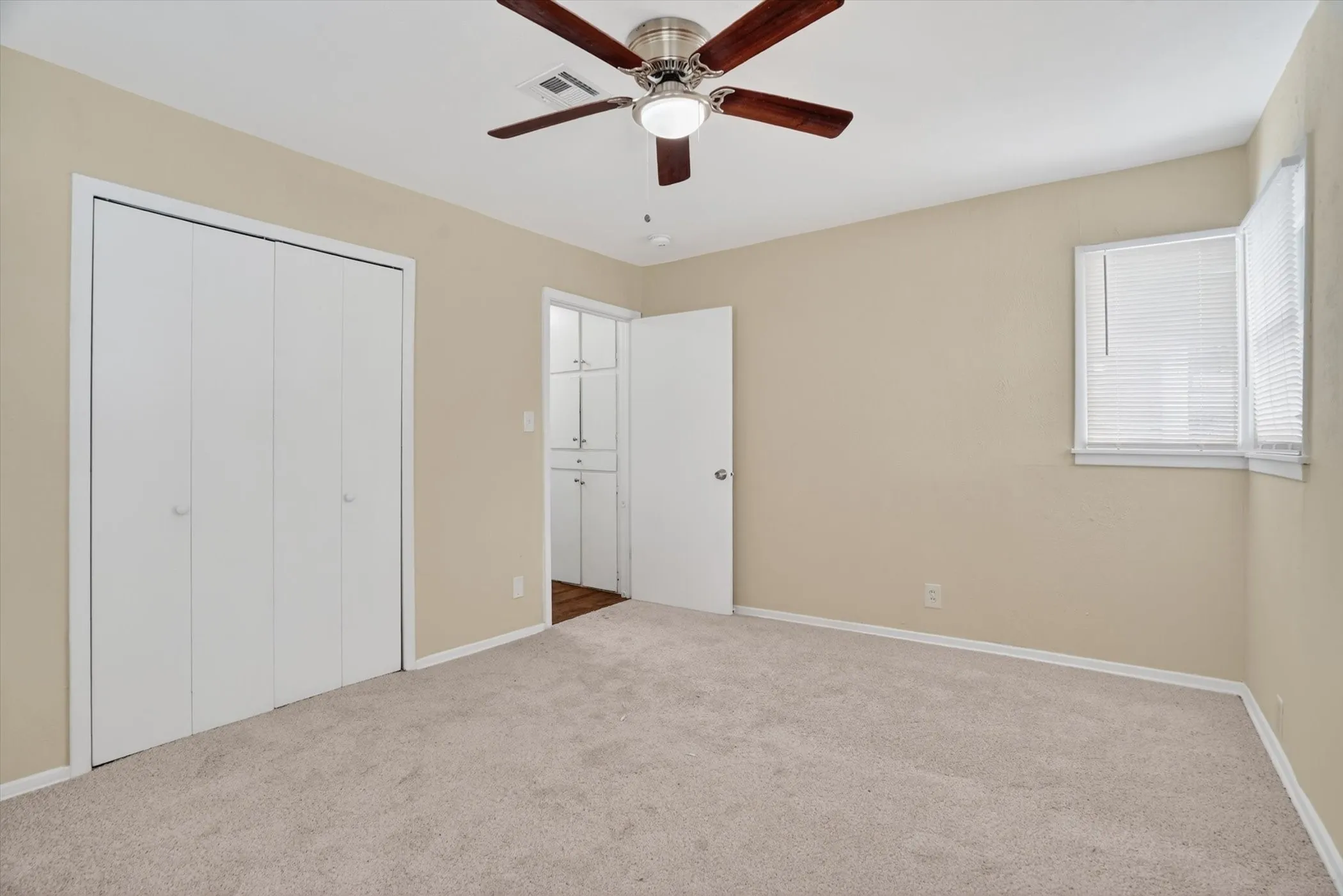 Carpeted interior space featuring a ceiling fan with integrated lighting, a window with horizontal blinds, and a closet with bifold doors