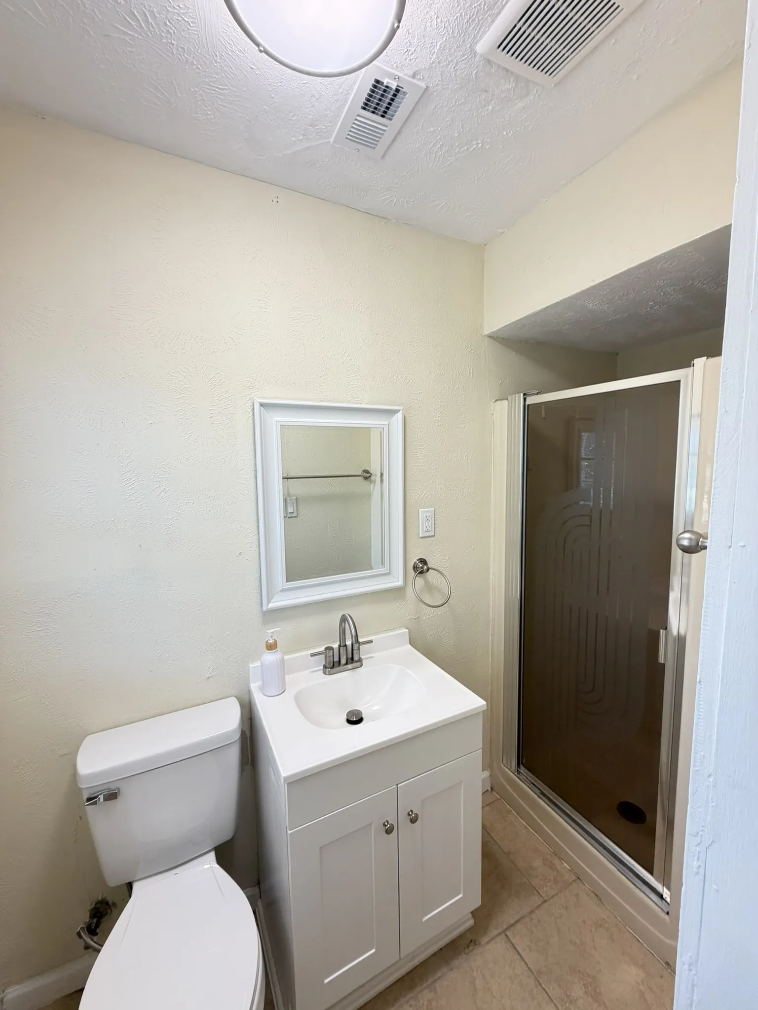 White vanity with a built-in sink, framed mirror, and a standing shower with a frosted glass enclosure