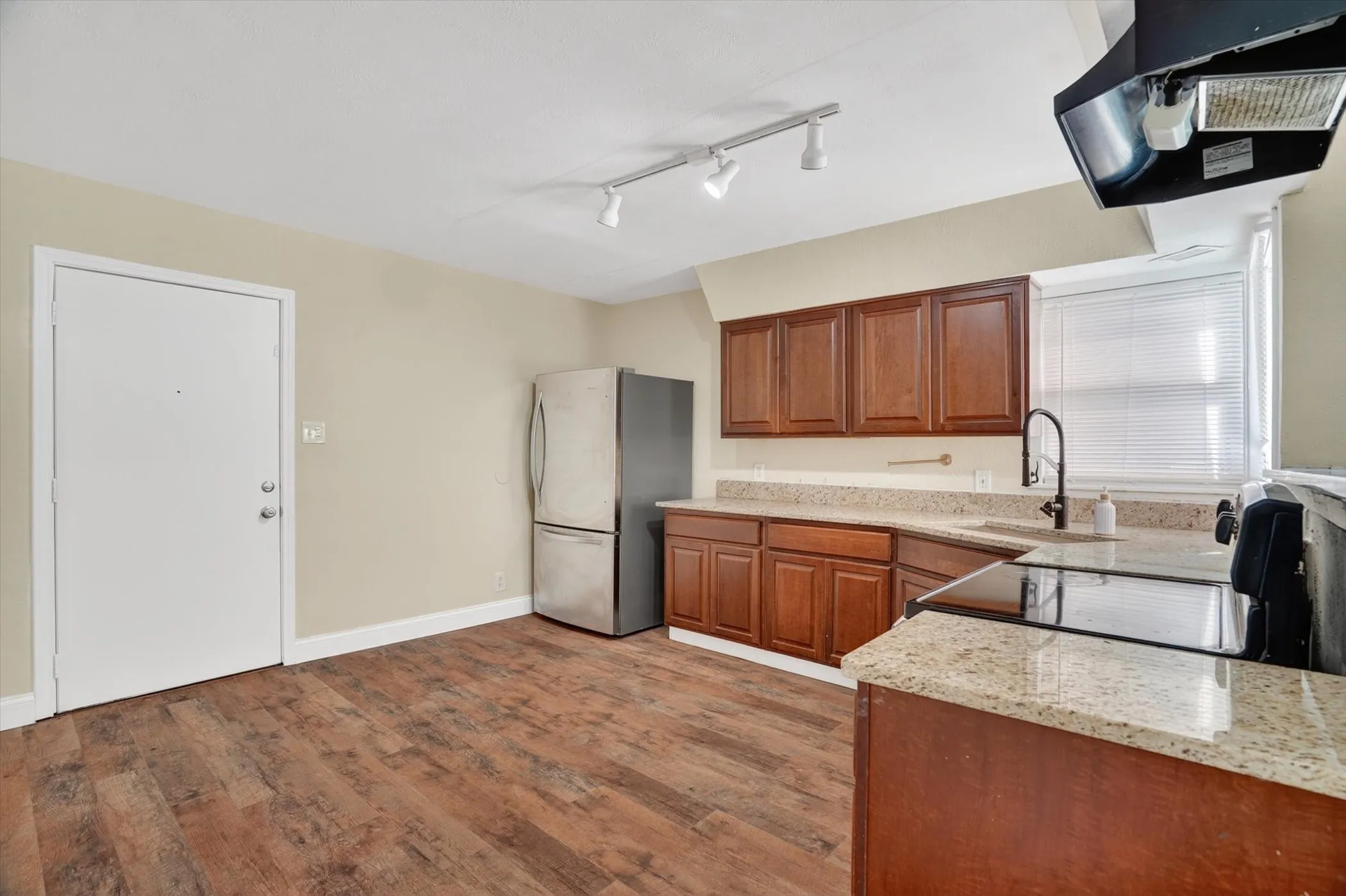 Kitchen featuring wood-finish flooring, wood cabinetry, stone countertops, and a stainless steel refrigerator