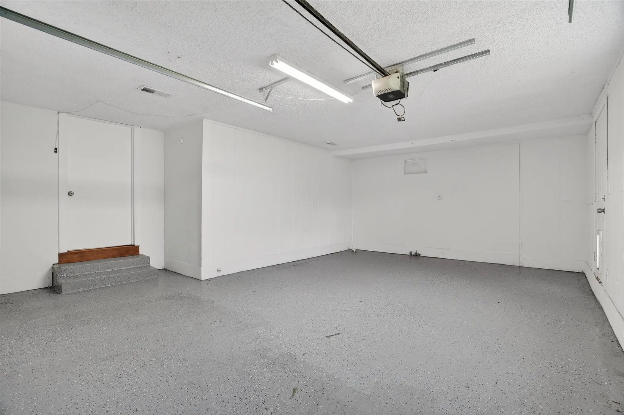 Spacious garage featuring a durable epoxy-coated concrete floor, white painted walls, and an automatic garage door opener system