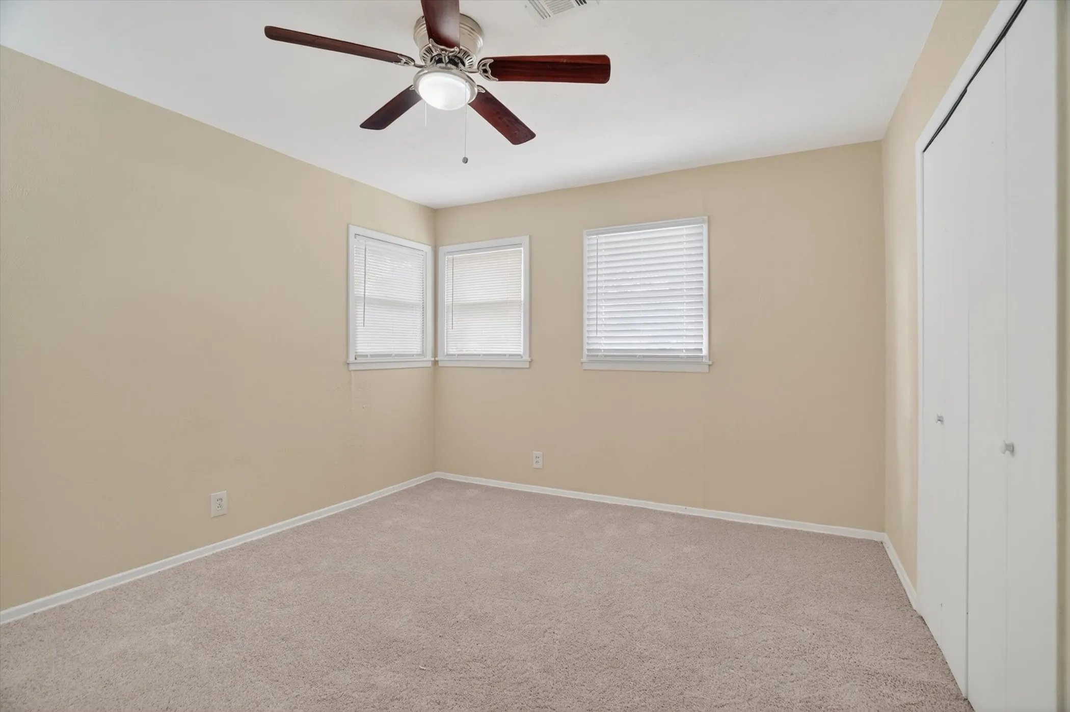 Carpeted room with two windows featuring blinds, a ceiling fan with integrated lighting, and a bi-fold door closet