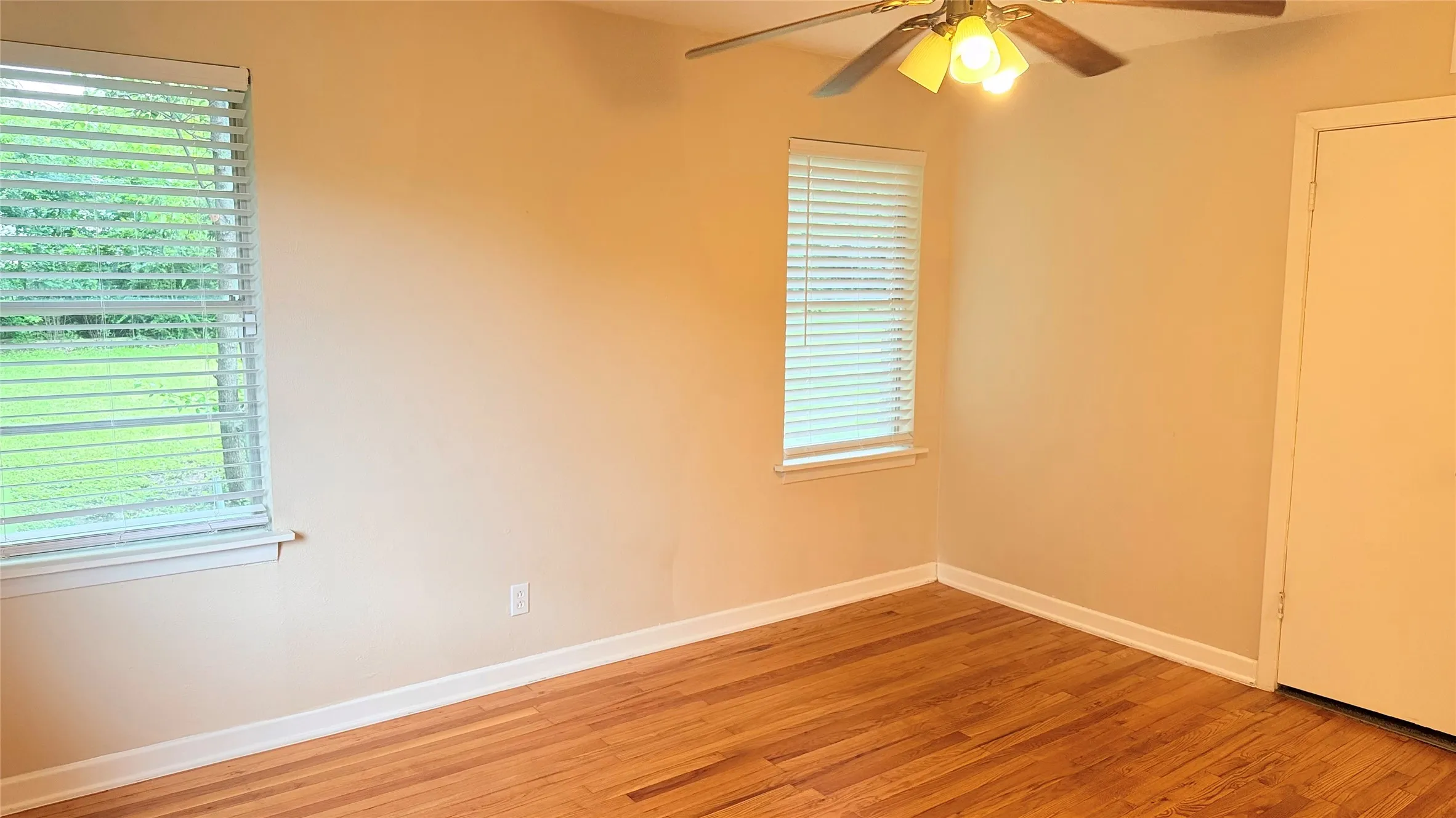 Room featuring warm-toned walls, wood flooring, white trim, two windows with blinds, and a ceiling fan with integrated lighting