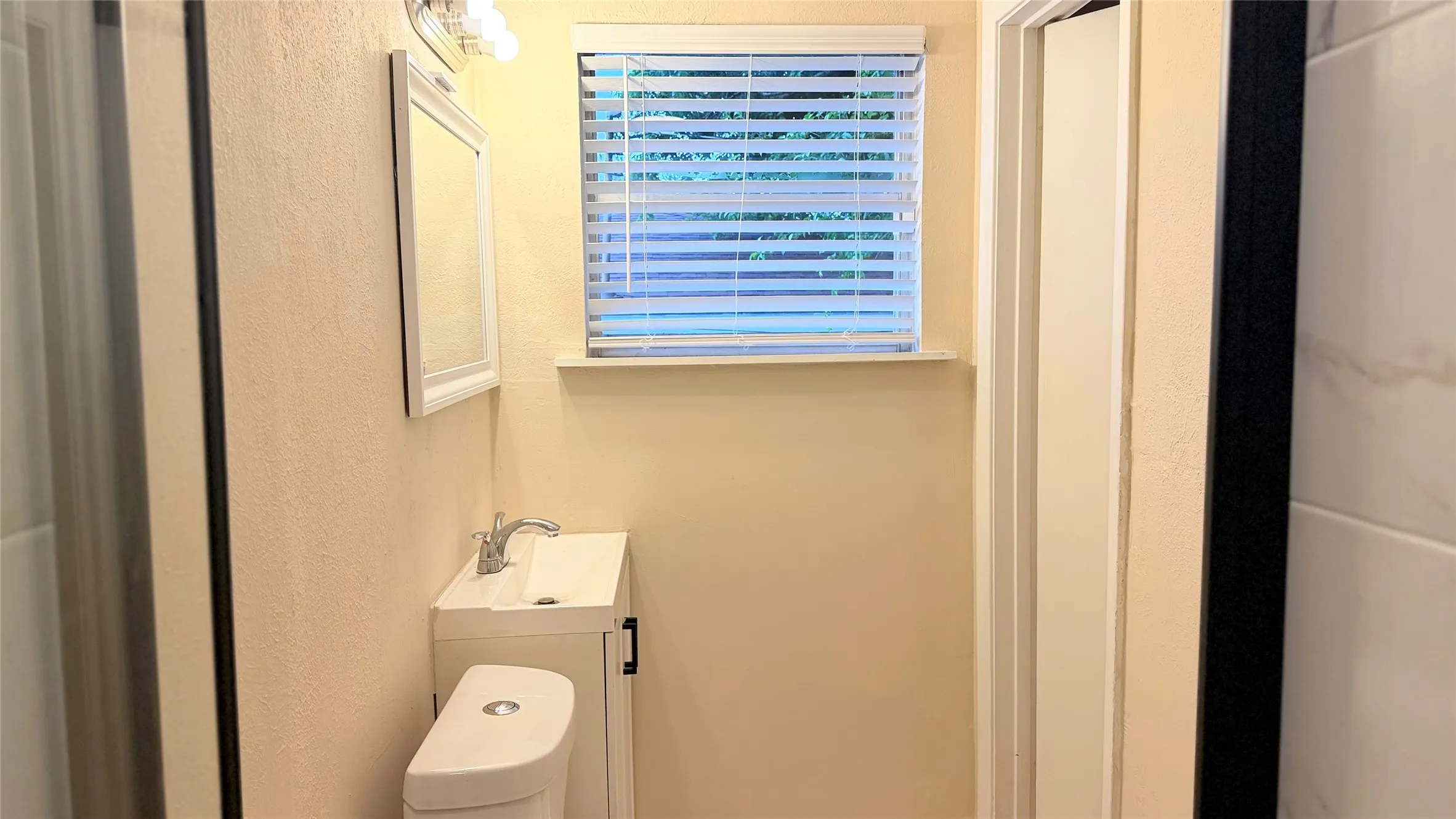 Bathroom with a single vanity, a window featuring blinds, a built-in toilet, and light-toned walls
