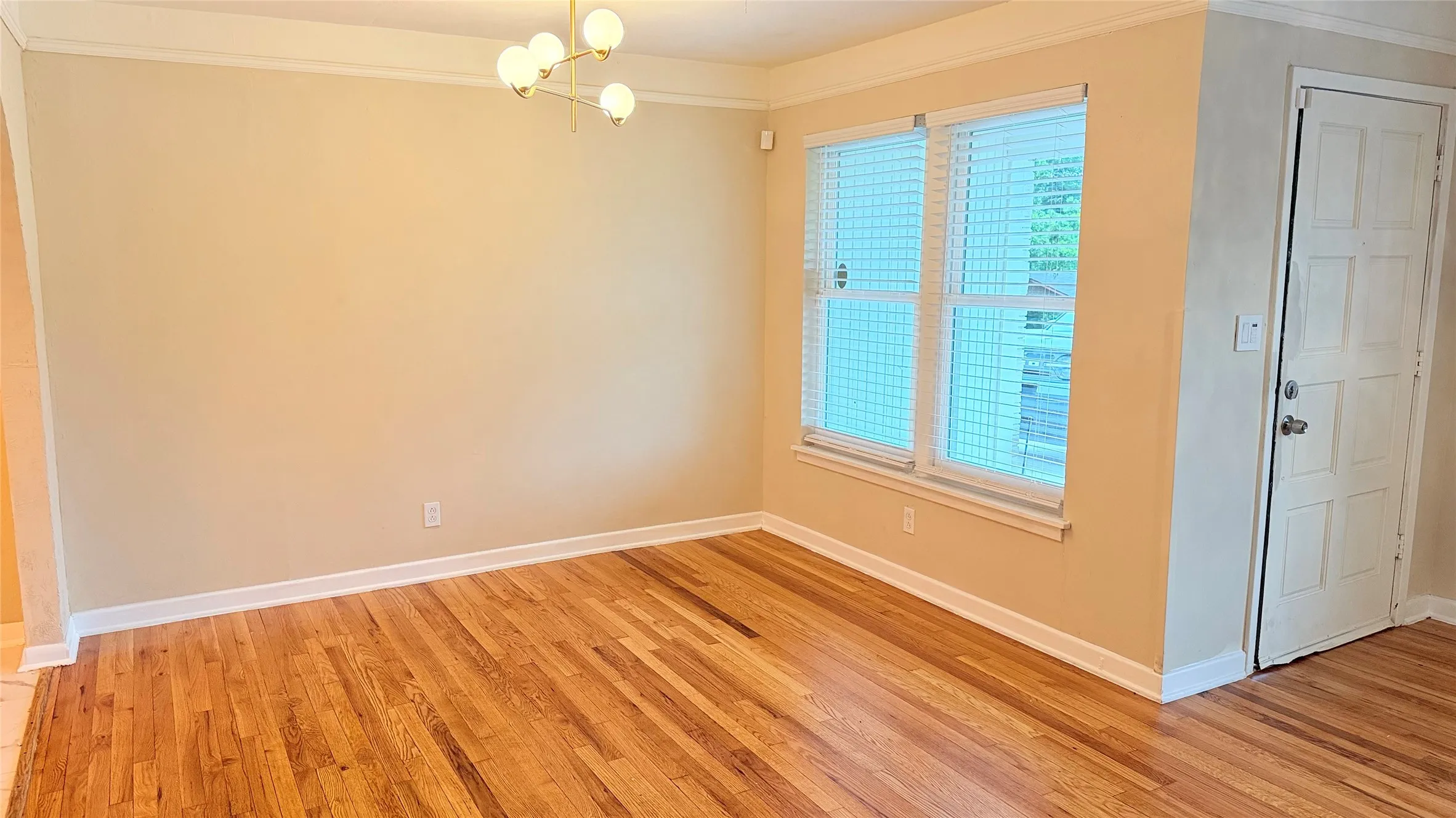 Hardwood flooring throughout featuring white baseboards, crown molding, and a modern chandelier