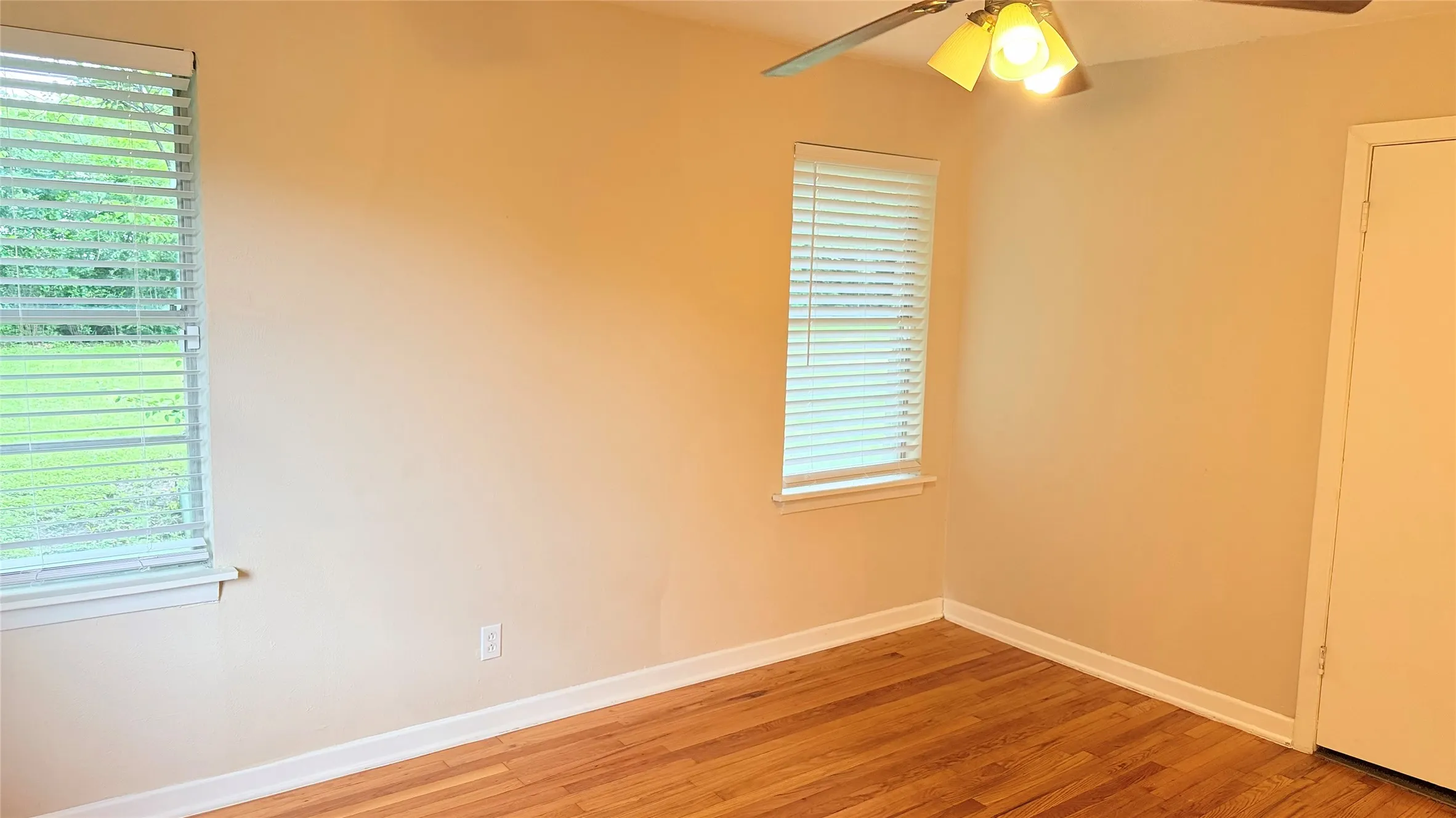 Hardwood flooring throughout featuring white baseboards, two windows with horizontal blinds, and a ceiling fan with integrated lighting
